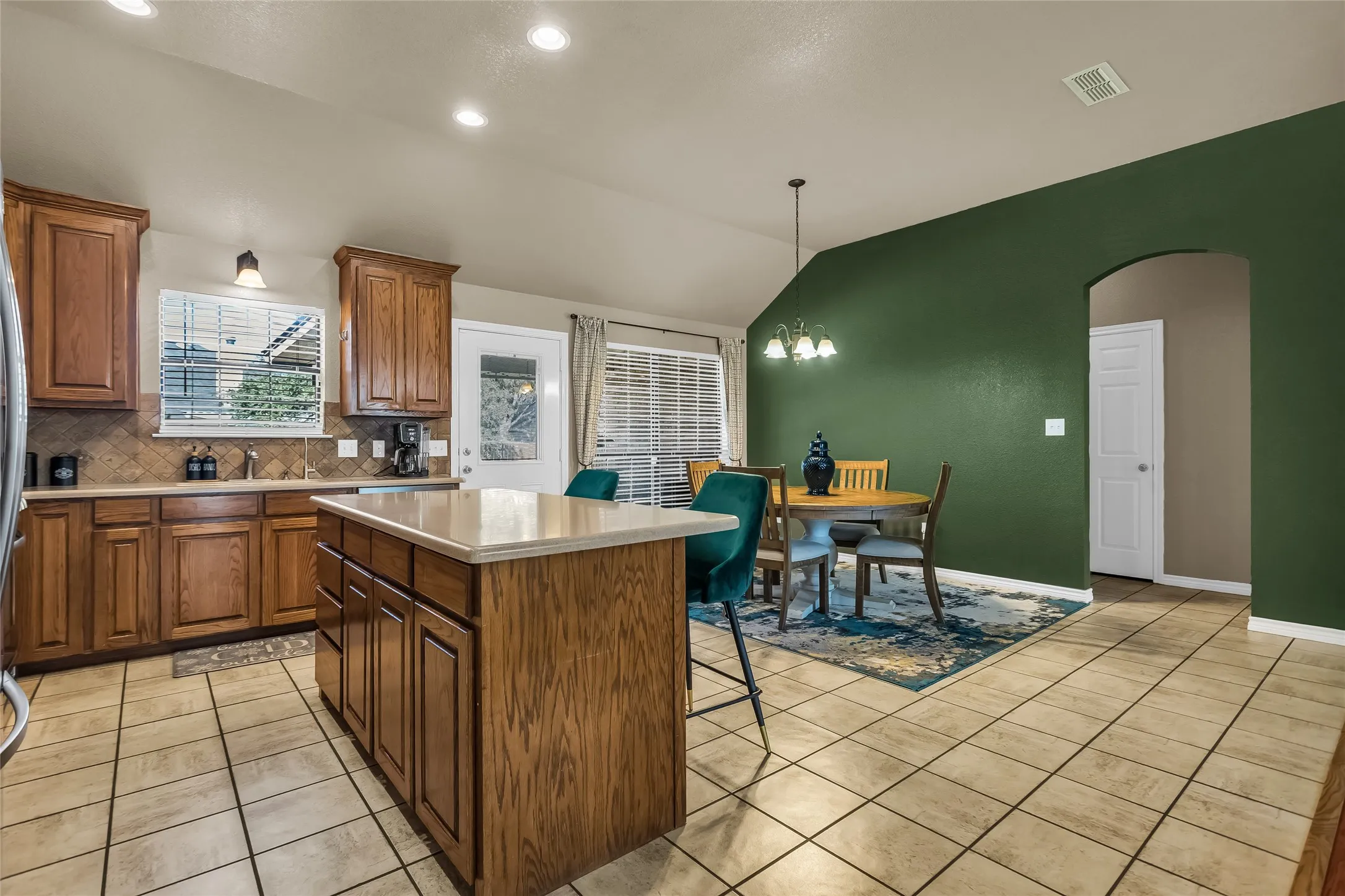 Kitchen featuring vaulted ceiling, brown cabinets, a center island, backsplash, and light tile patterned floors