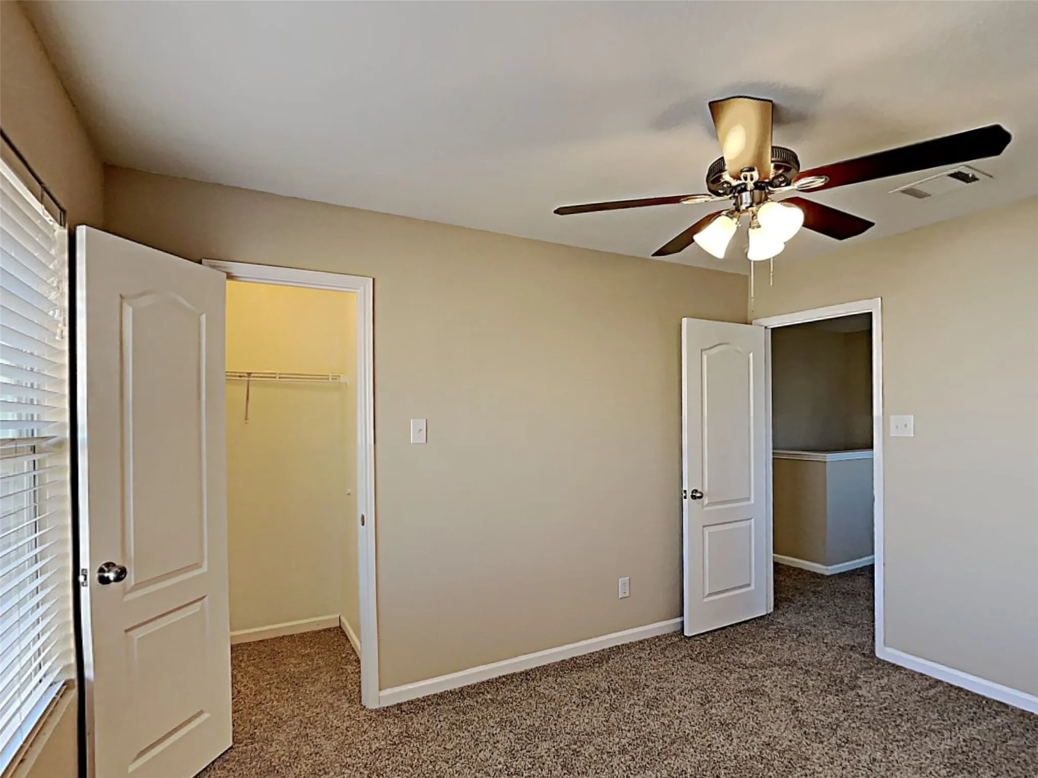 Unfurnished bedroom featuring dark colored carpet, a walk in closet, and ceiling fan