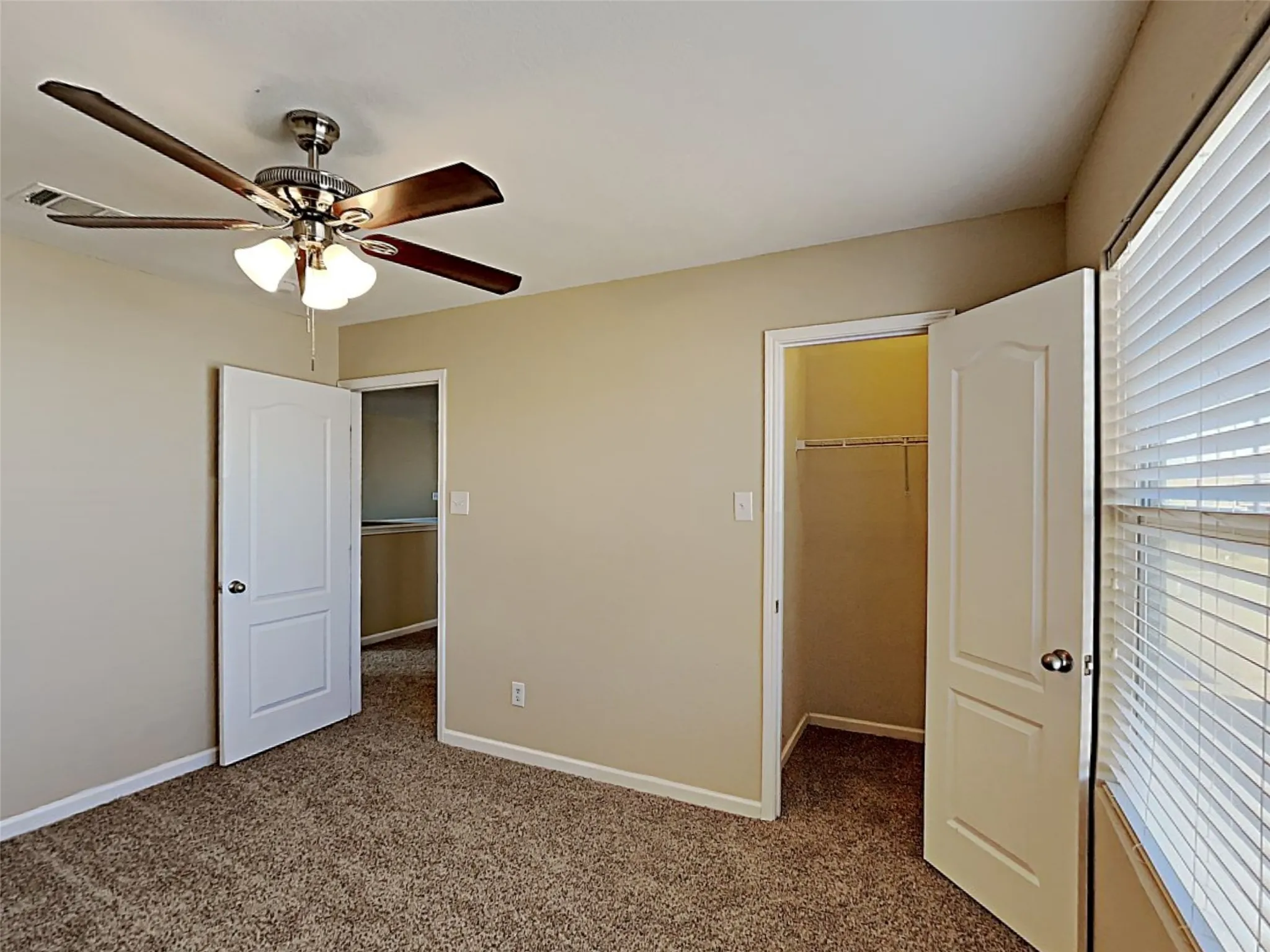 Unfurnished bedroom featuring dark carpet, a spacious closet, and a ceiling fan