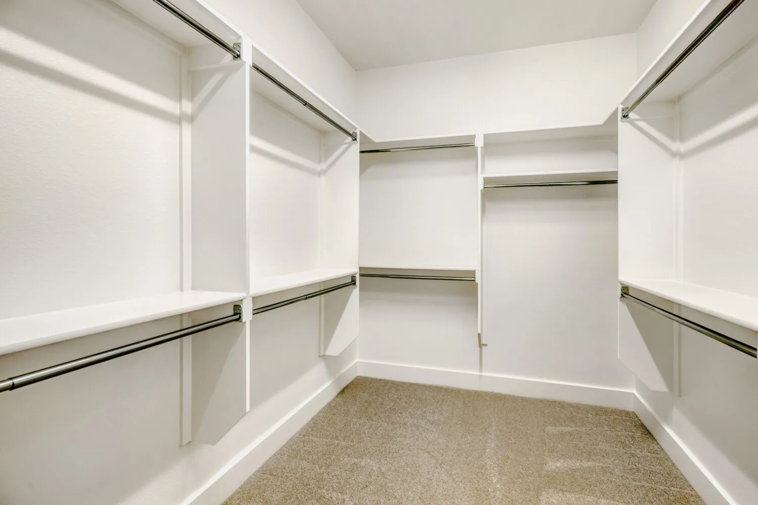 Walk-in closet featuring white built-in shelving, multiple hanging rods, and carpet flooring