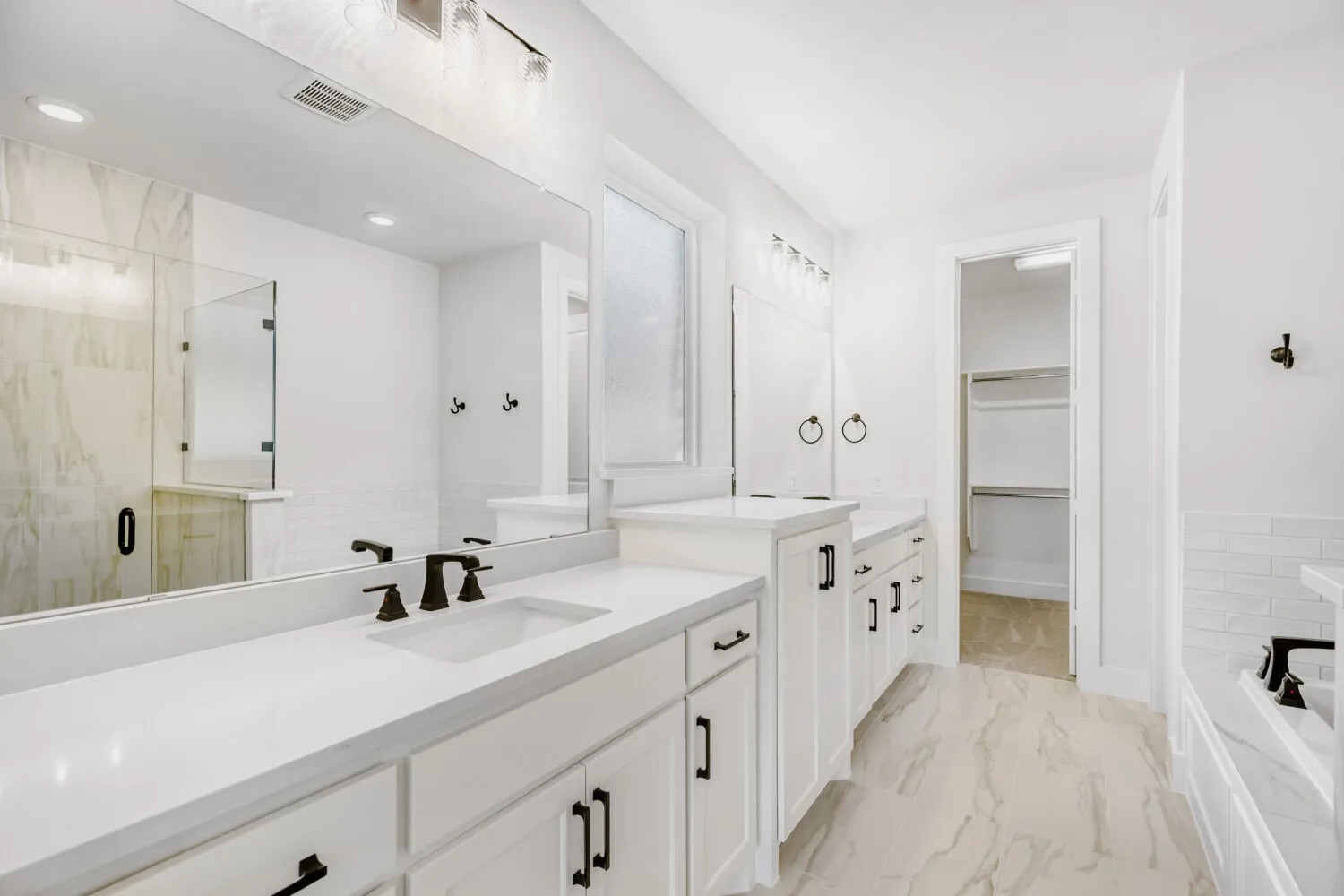 Bright bathroom featuring dual vanities with white cabinetry and countertops