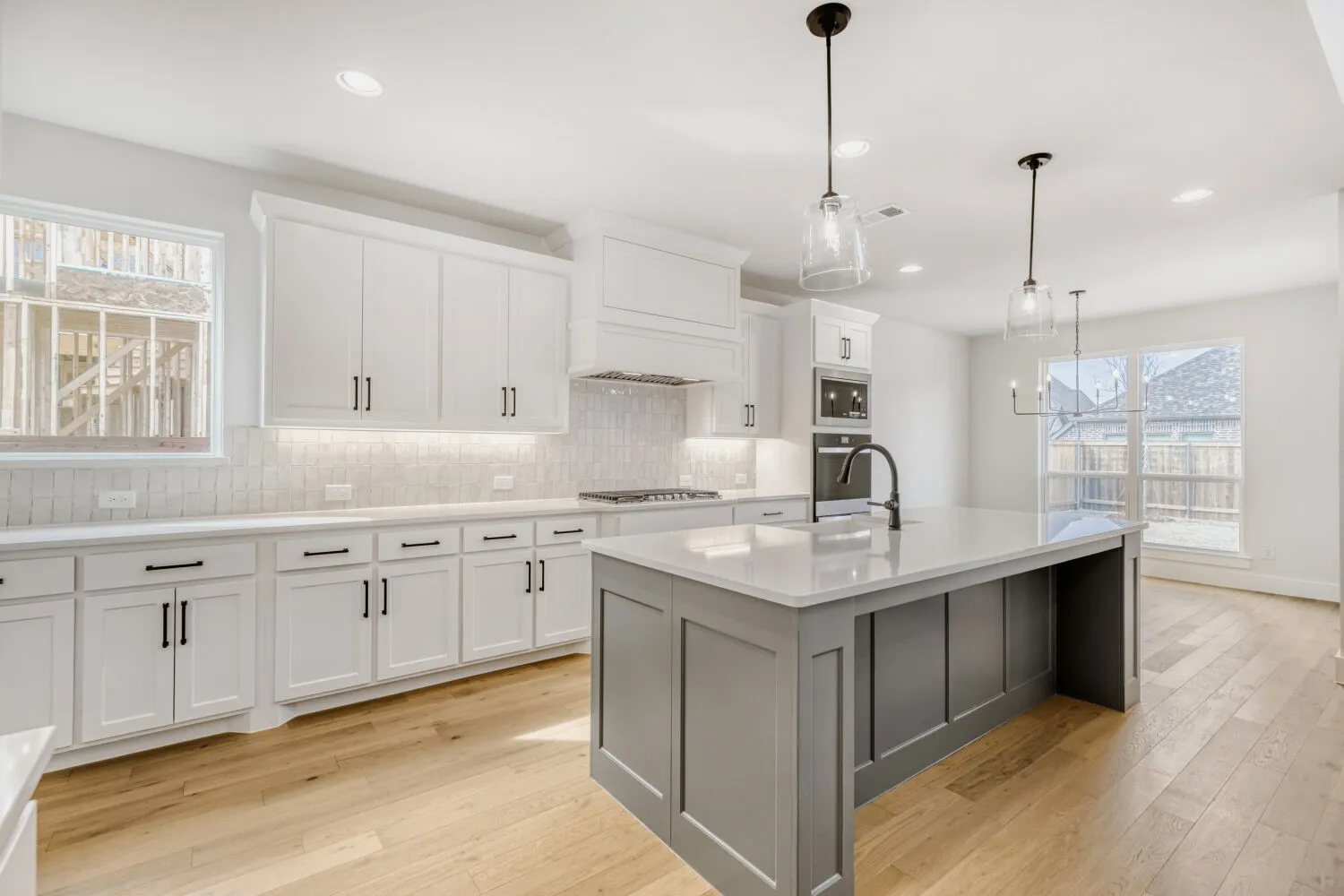 Open-concept kitchen featuring an expansive center island with seating, white shaker cabinetry, a subway tile backsplash, stainless steel appliances, and wood-finish flooring