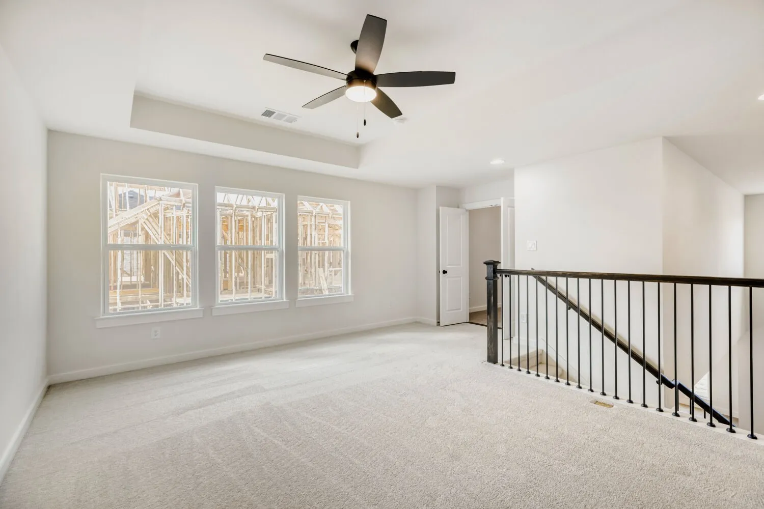Spacious upper-level loft featuring light-toned carpeting, a contemporary ceiling fan, and a tray ceiling