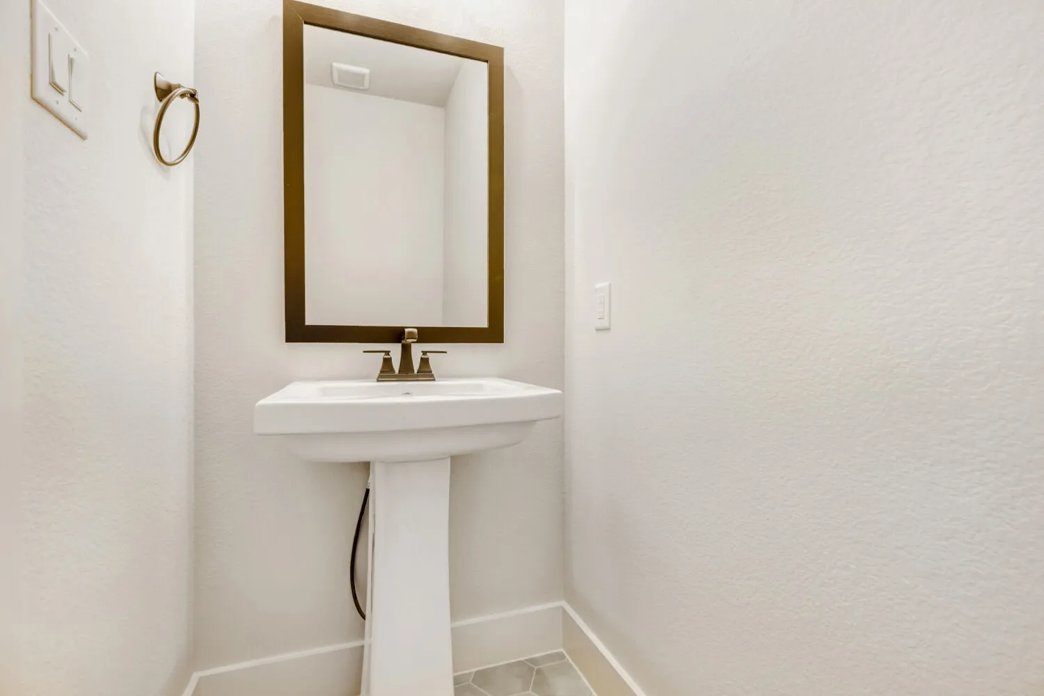 White pedestal sink with a bronze-framed mirror and matching bronze faucet