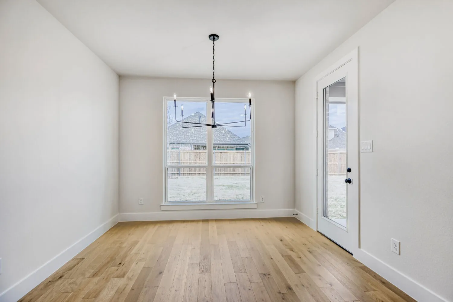 Spacious room featuring wood-finish flooring, a contemporary black chandelier, and a large window providing ample natural light