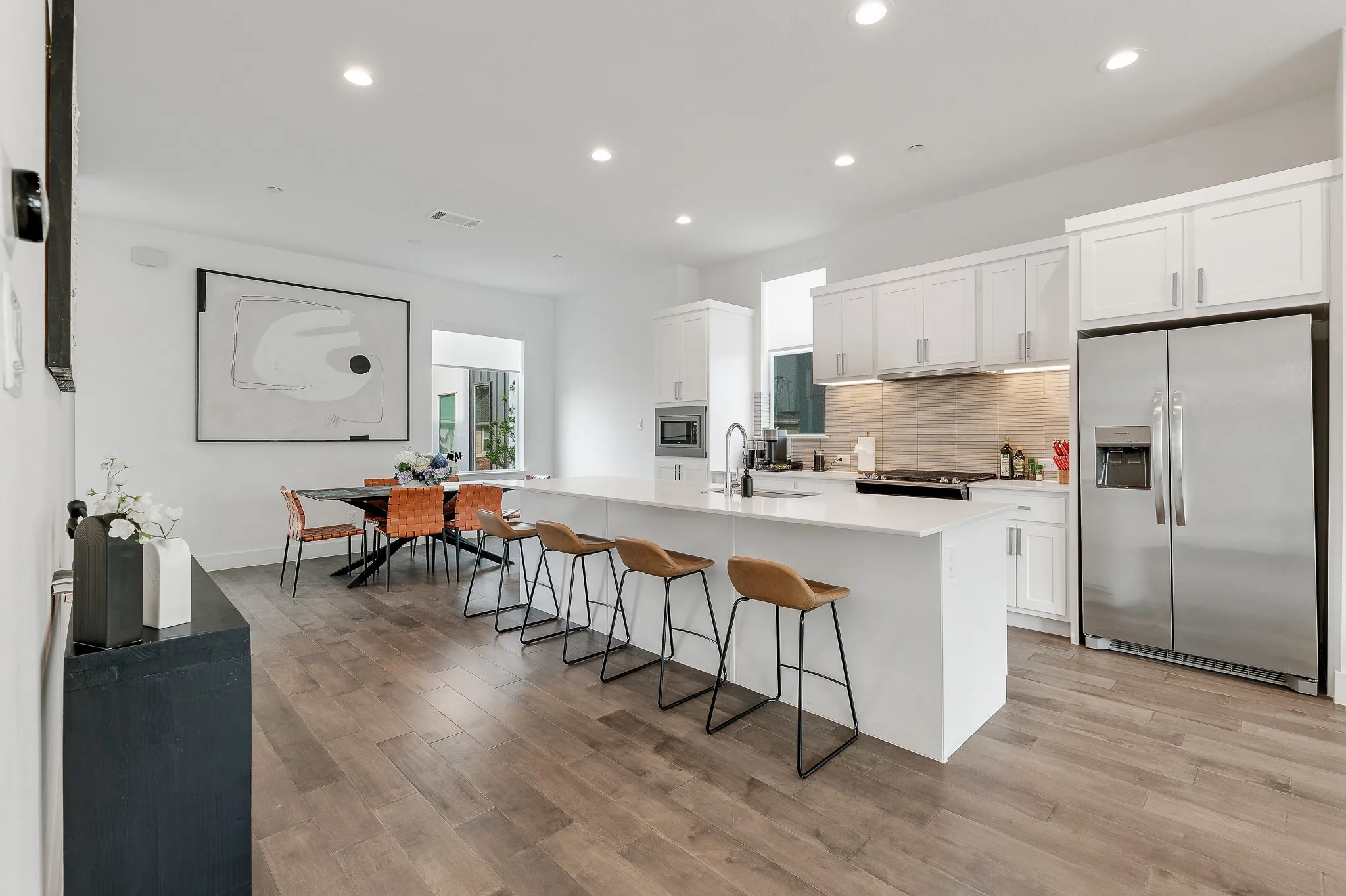 Kitchen with stainless steel appliances, backsplash, white cabinets, recessed lighting, and an island with sink