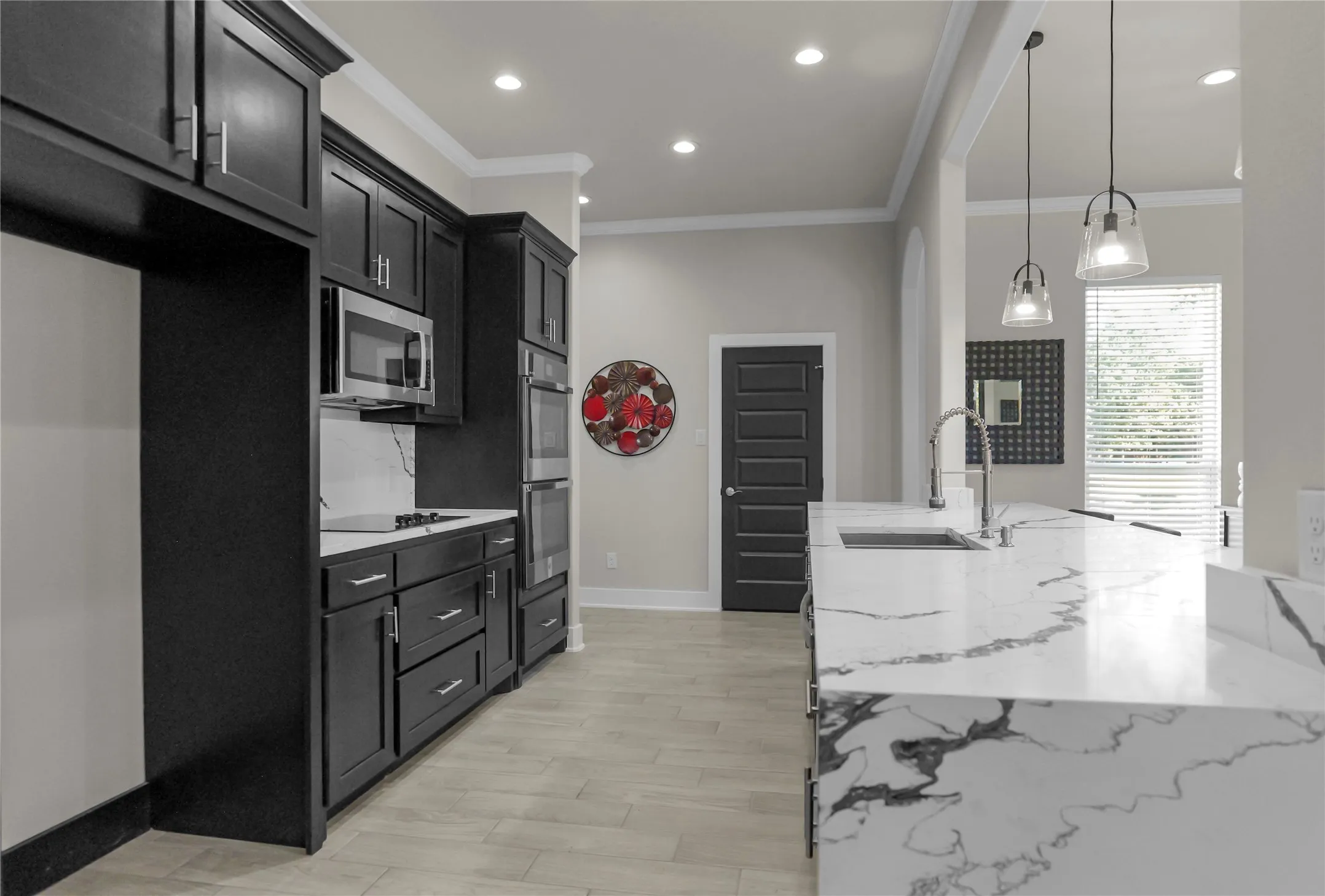 Kitchen featuring light stone counters, ornamental molding, dark cabinets, pendant lighting, and light wood-type flooring