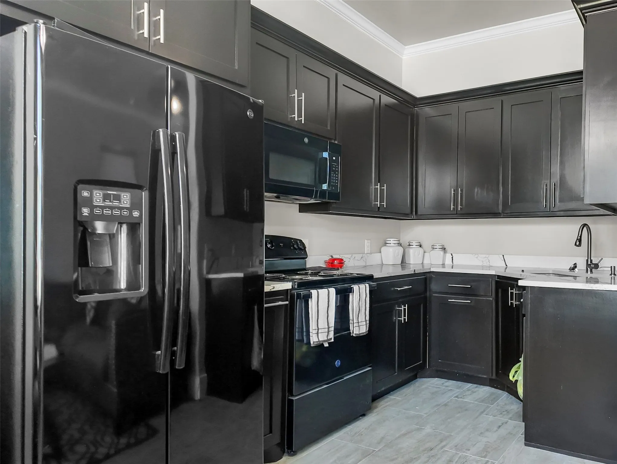 Kitchen featuring black appliances, crown molding, dark cabinetry, and light stone counters
