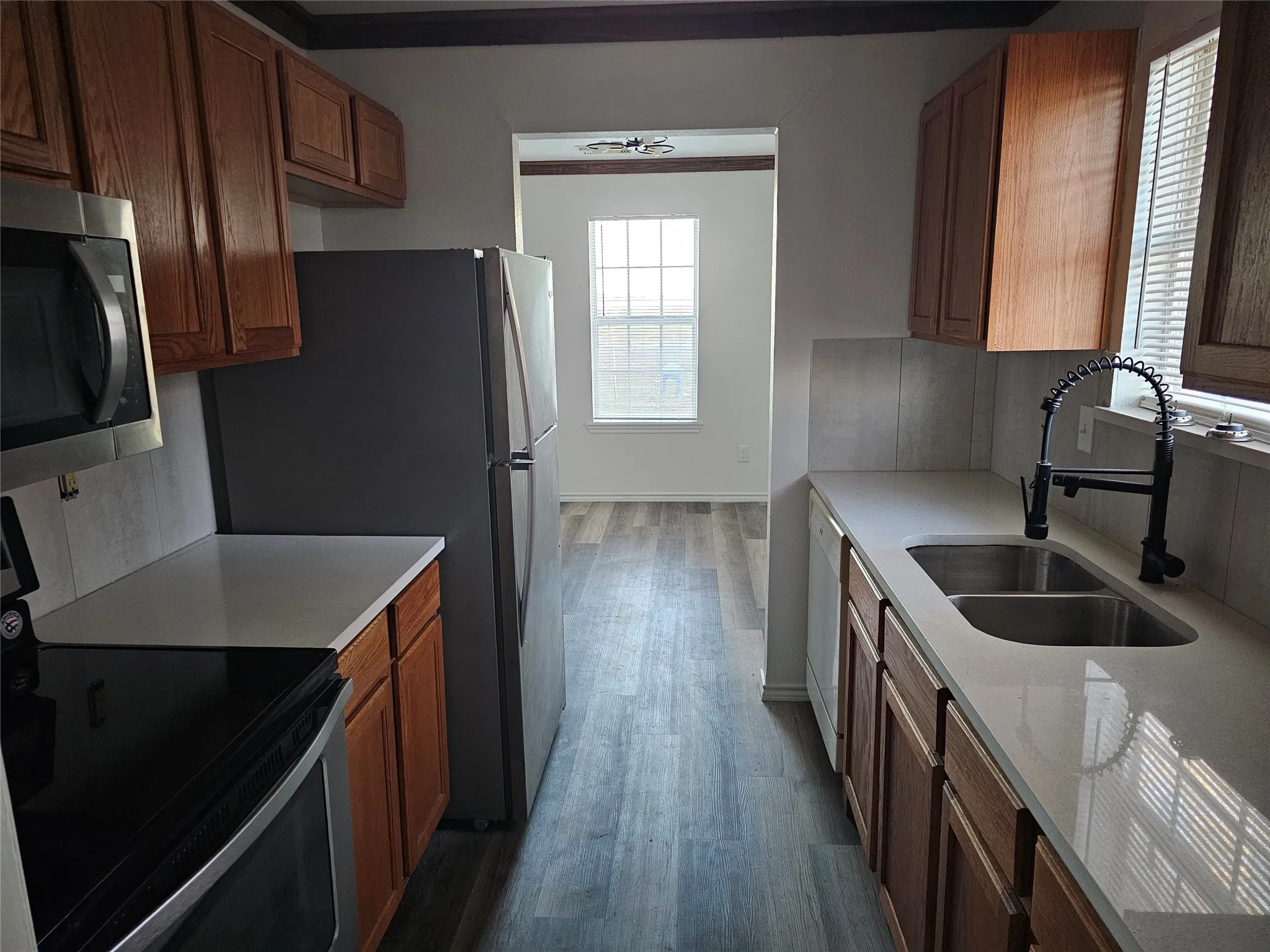 Kitchen with appliances with stainless steel finishes, dark wood-type flooring, brown cabinetry, and light stone countertops