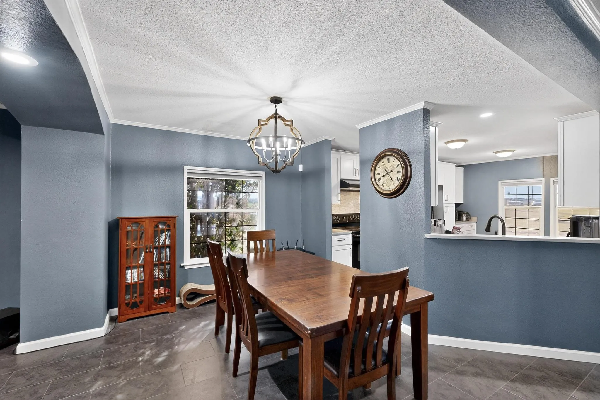 Dining area with a textured ceiling, a chandelier, a textured wall, crown molding, and dark tile patterned floors