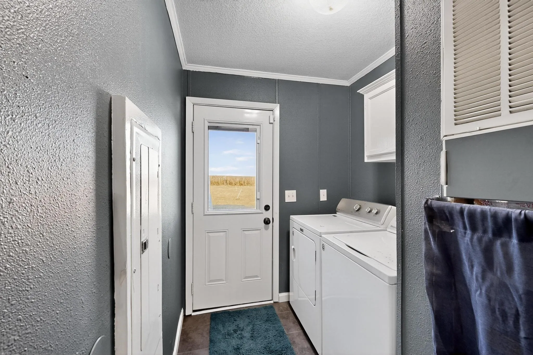 Washroom featuring crown molding, a textured wall, dark tile patterned floors, a textured ceiling, and cabinet space