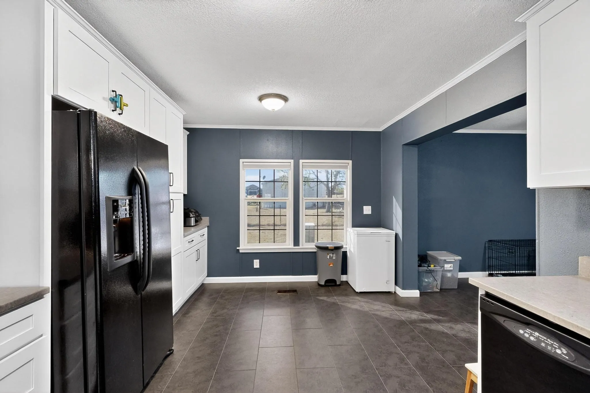 Kitchen featuring black appliances, ornamental molding, white cabinets, dark tile patterned floors, and a textured ceiling
