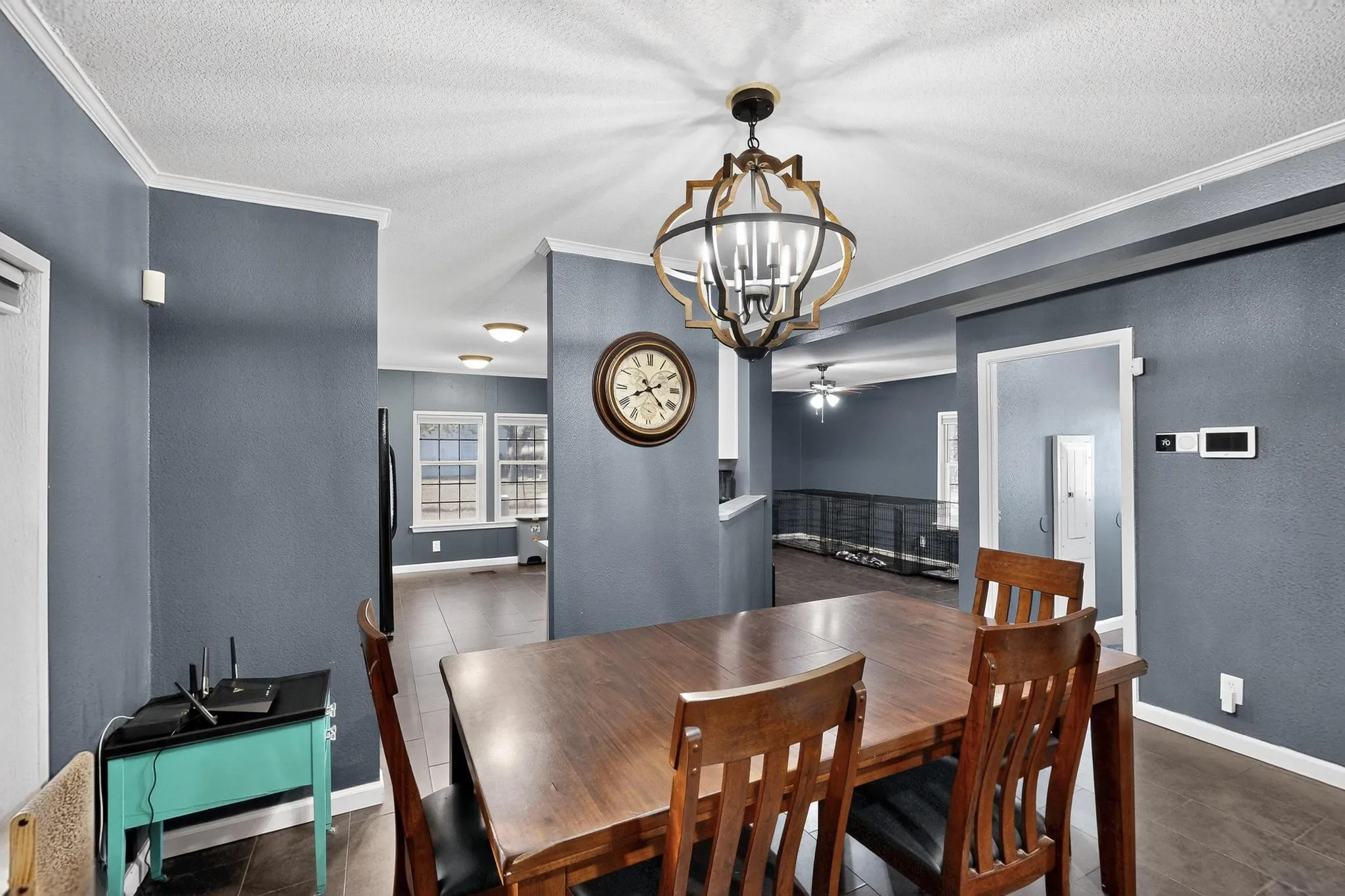 Dining area with a textured wall, a textured ceiling, ornamental molding, a chandelier, and dark tile patterned flooring