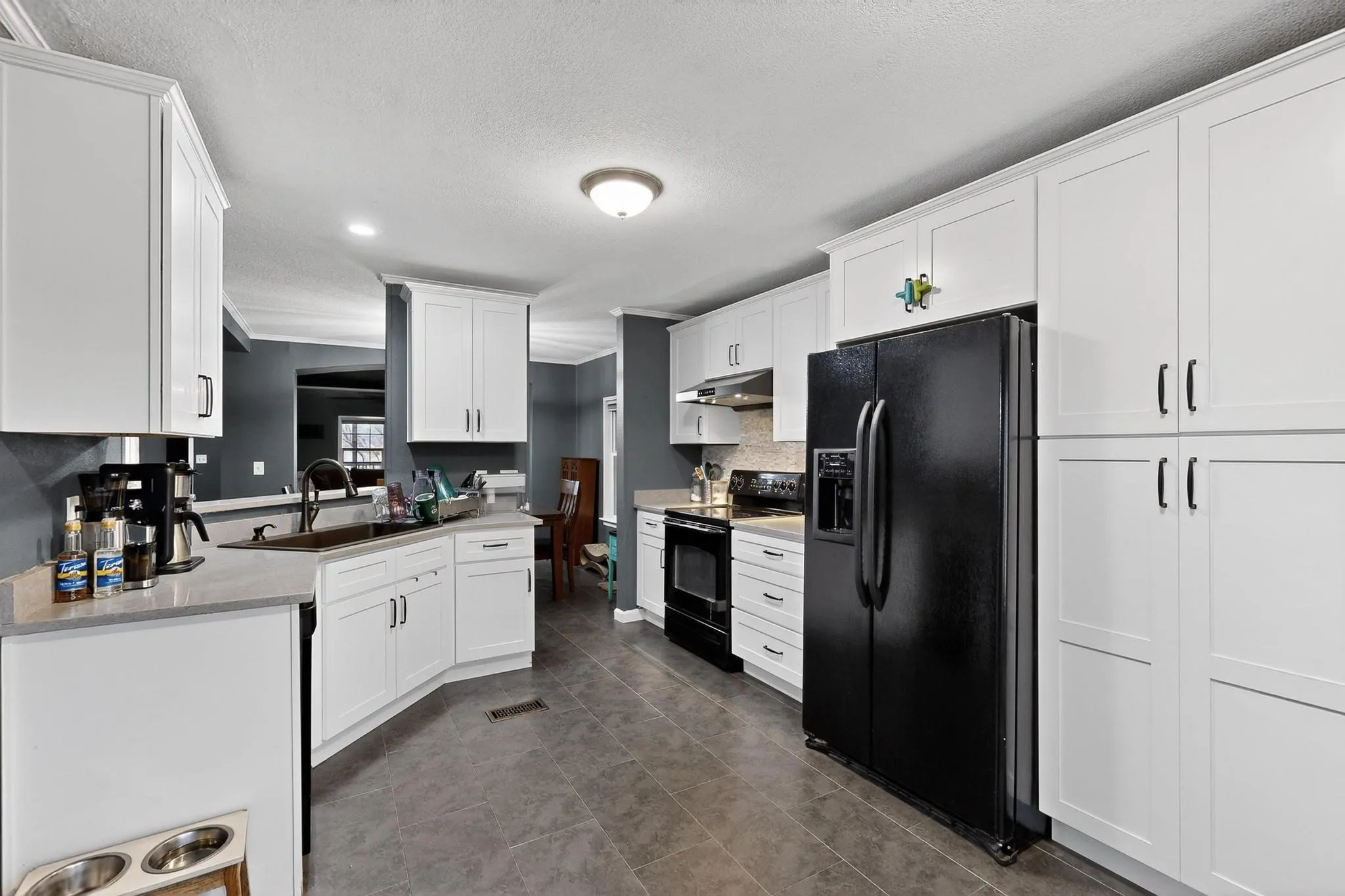 Kitchen featuring black appliances, white cabinetry, a textured ceiling, dark tile patterned floors, and under cabinet range hood
