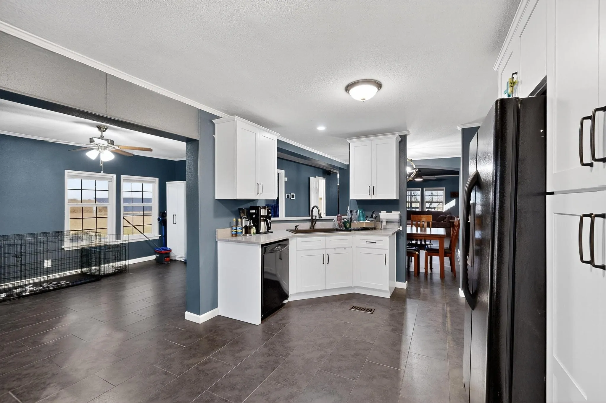 Kitchen with ceiling fan, white cabinetry, black appliances, light countertops, and ornamental molding