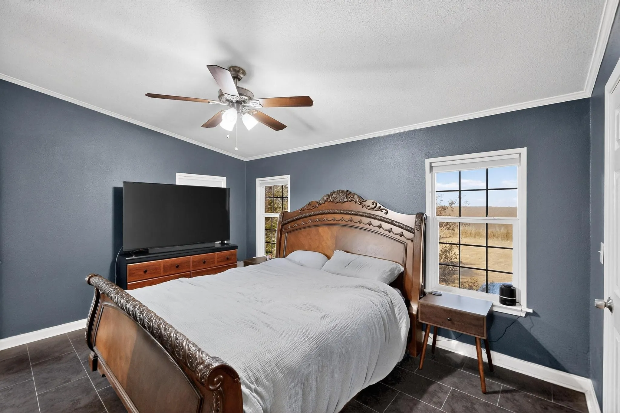 Bedroom with ornamental molding, ceiling fan, a textured wall, and dark tile patterned floors