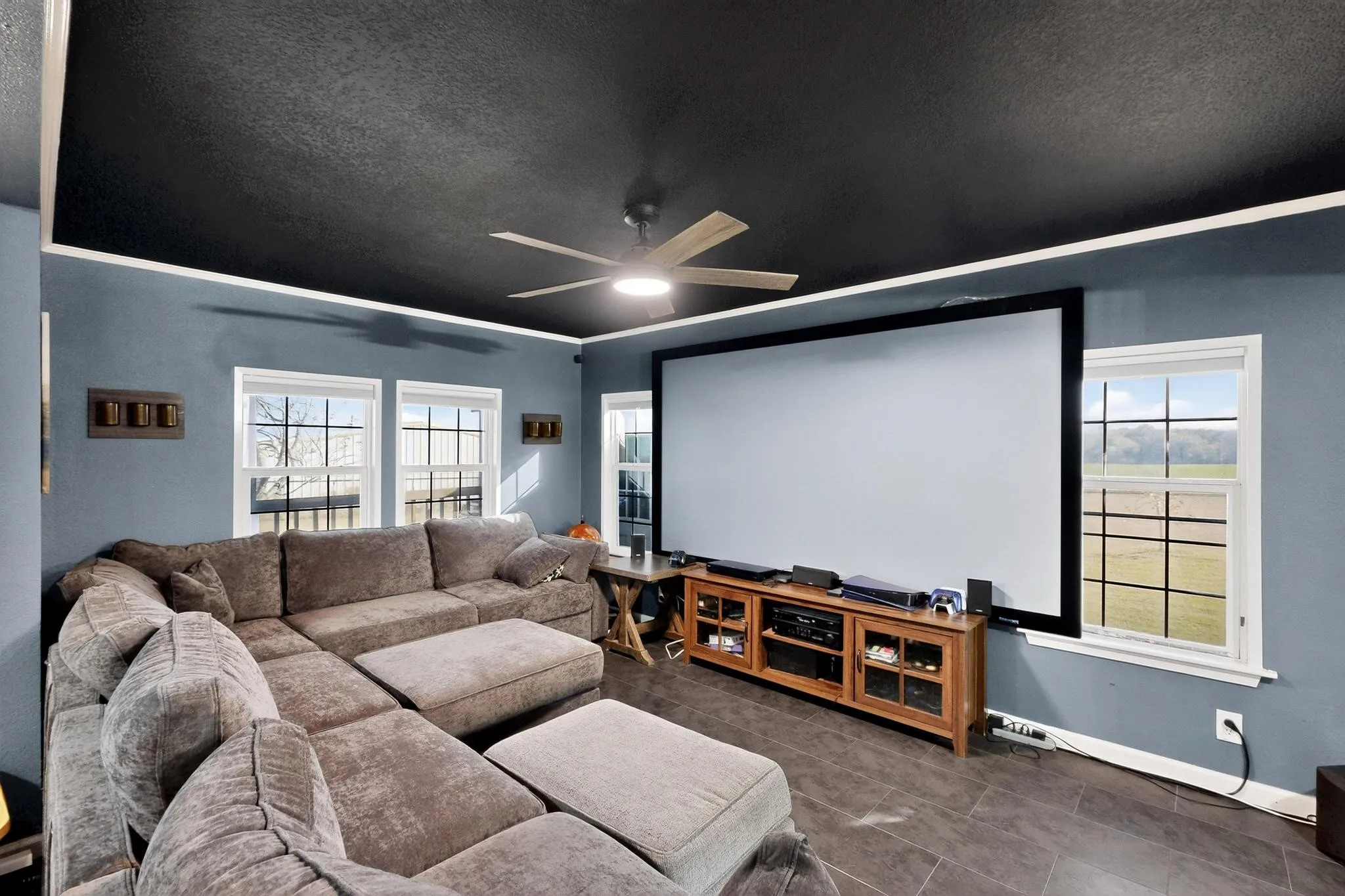 Cinema room featuring a textured ceiling, healthy amount of natural light, dark tile patterned floors, and ceiling fan