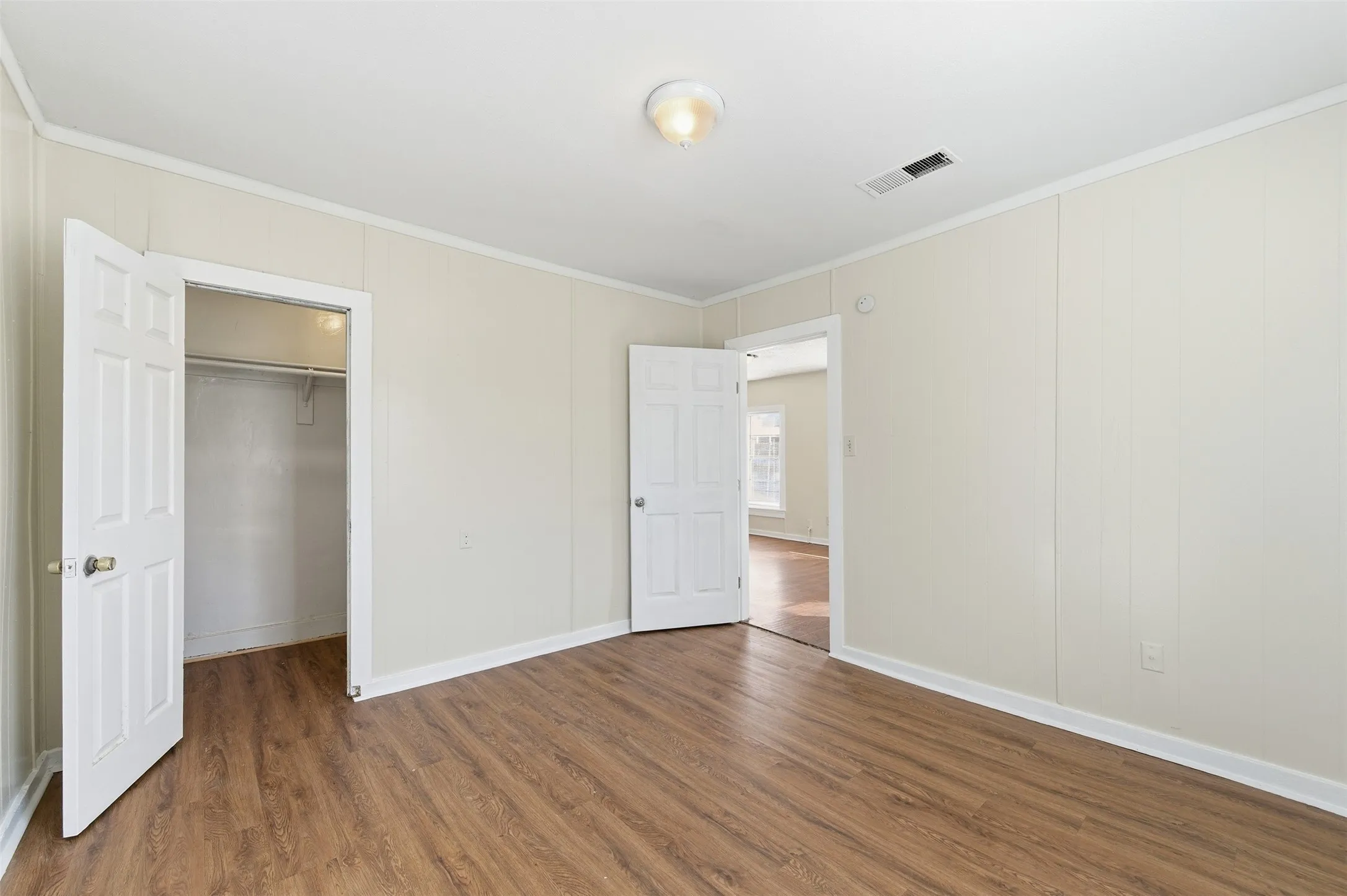 Unfurnished bedroom with crown molding, a spacious closet, and dark wood-type flooring