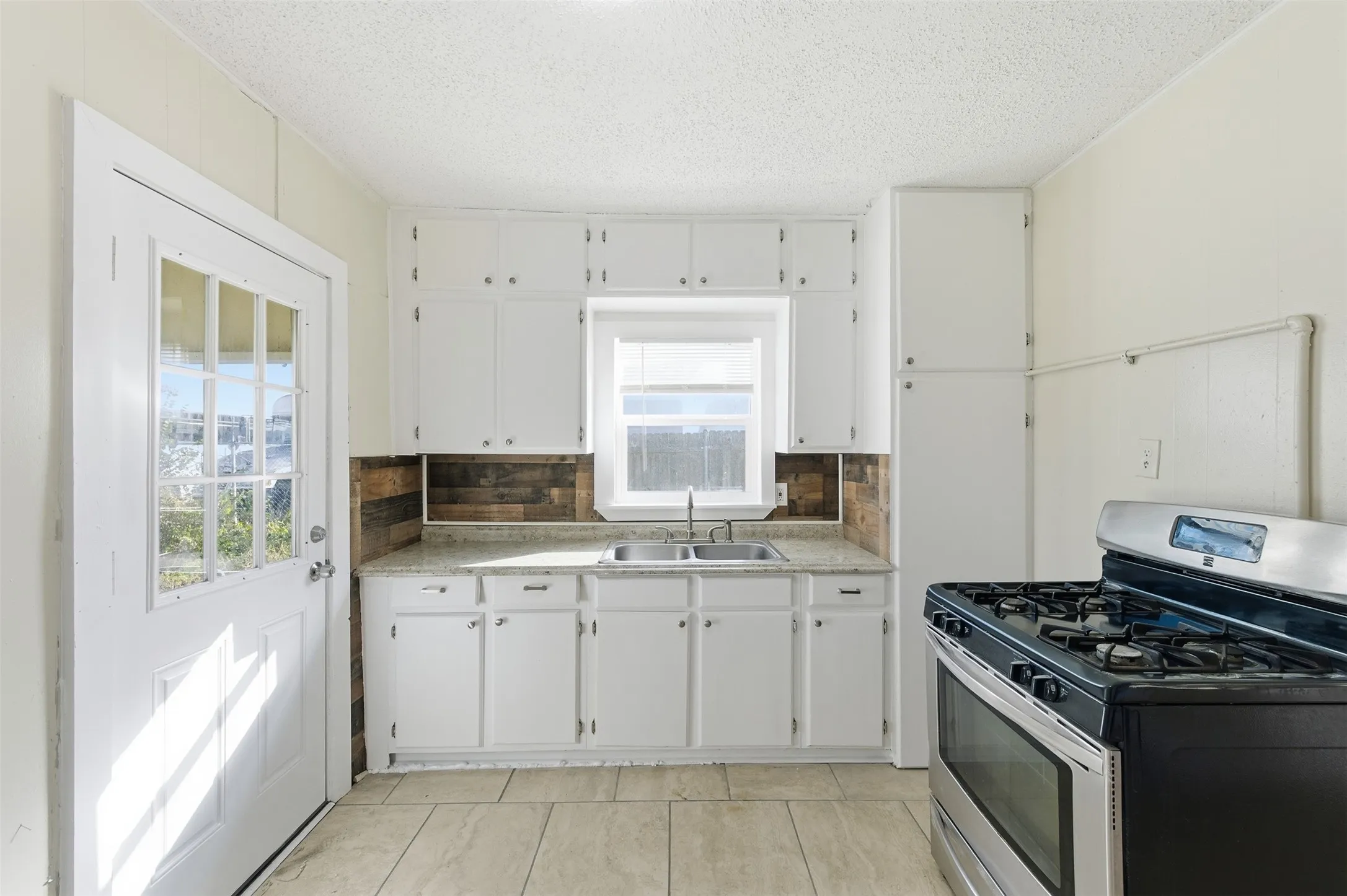 Kitchen featuring stainless steel range with gas stovetop, light countertops, white cabinets, tasteful backsplash, and a textured ceiling