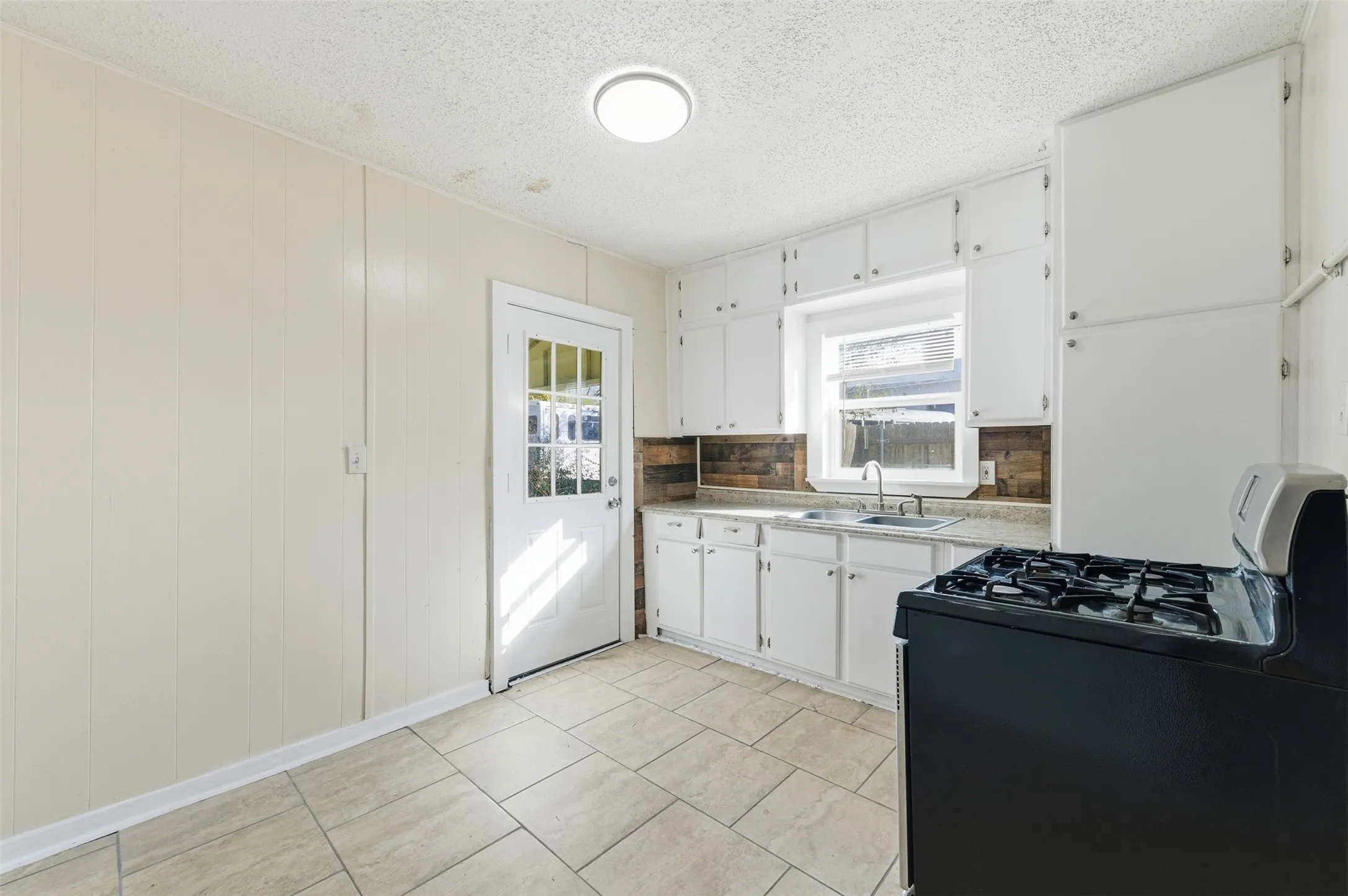 Kitchen with black range with gas cooktop, white cabinets, a textured ceiling, light tile patterned floors, and decorative backsplash