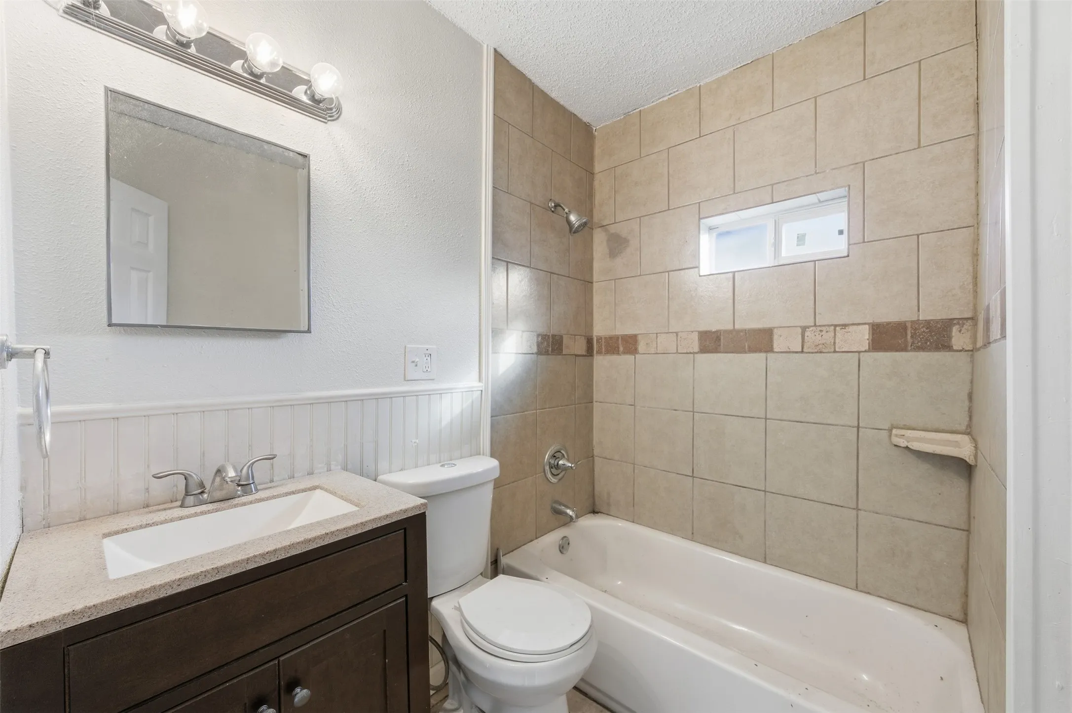 Bathroom featuring shower / washtub combination, vanity, wainscoting, a textured ceiling, and a textured​​‌​​​​‌​​‌‌​‌‌​​​‌‌​‌​‌​‌​​​‌​​ wall