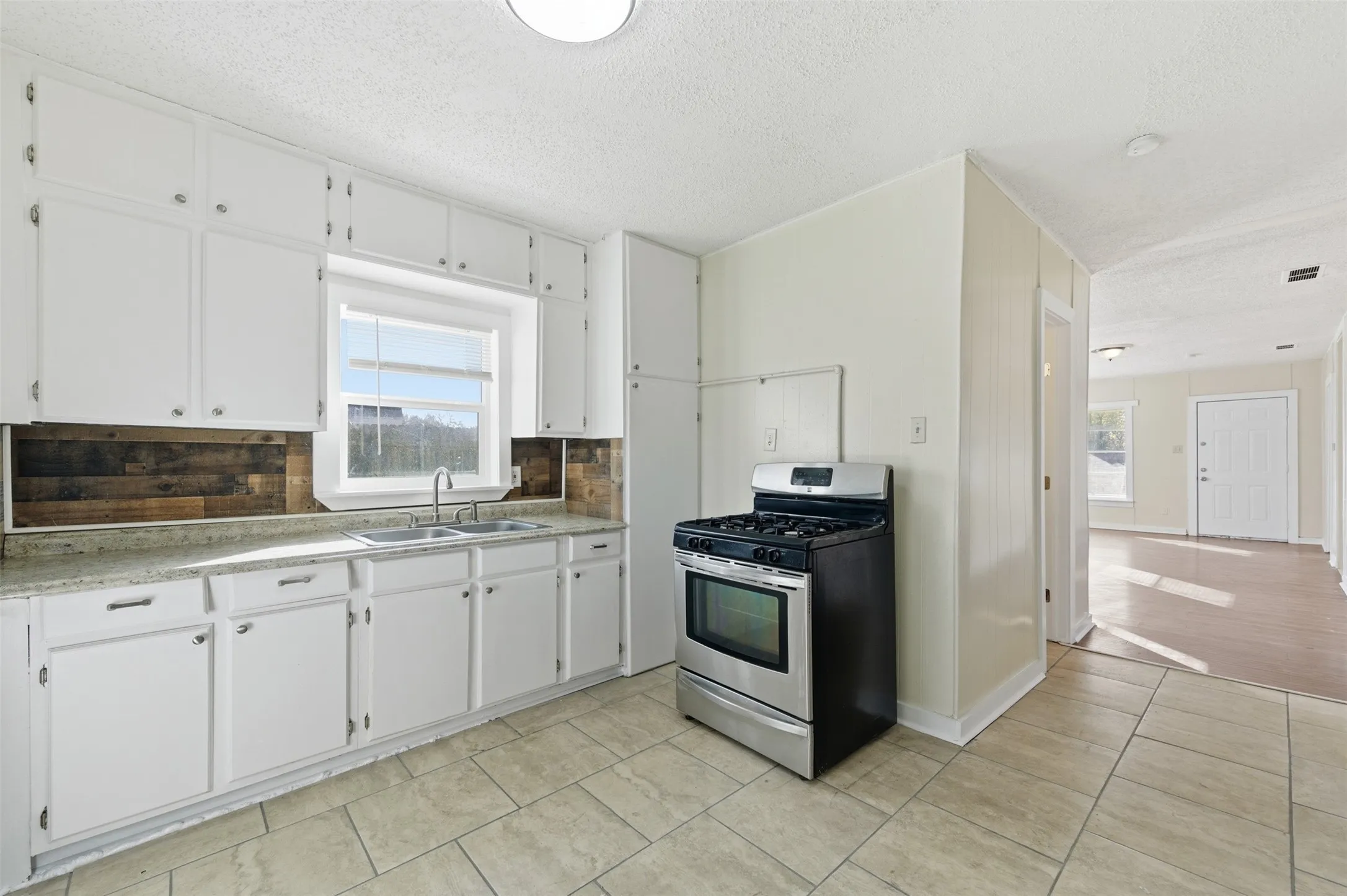 Kitchen featuring stainless steel gas range oven, white cabinetry, light countertops, a textured ceiling, and decorative backsplash
