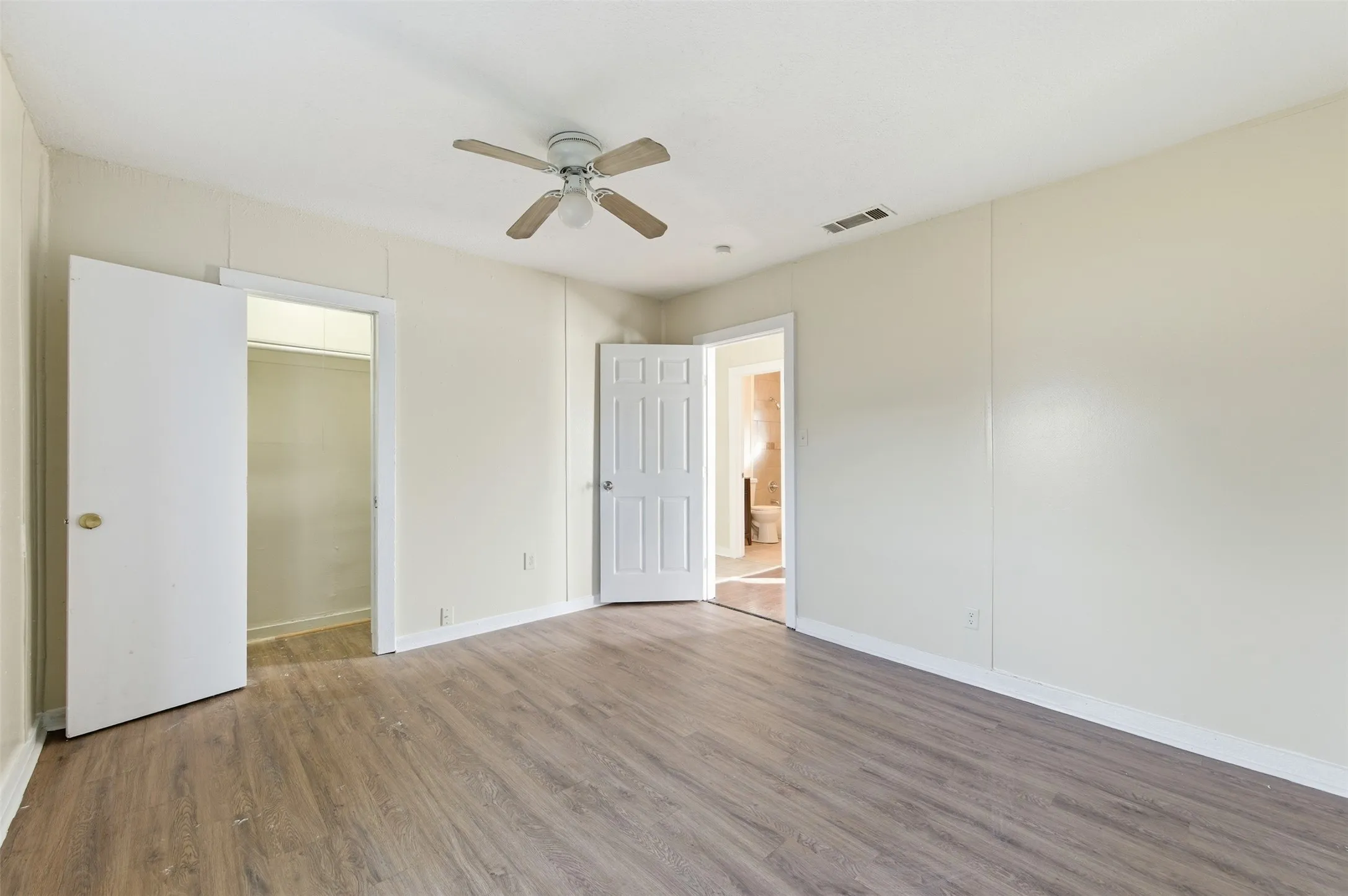 Unfurnished bedroom featuring wood finished floors, a walk in closet, and a ceiling fan