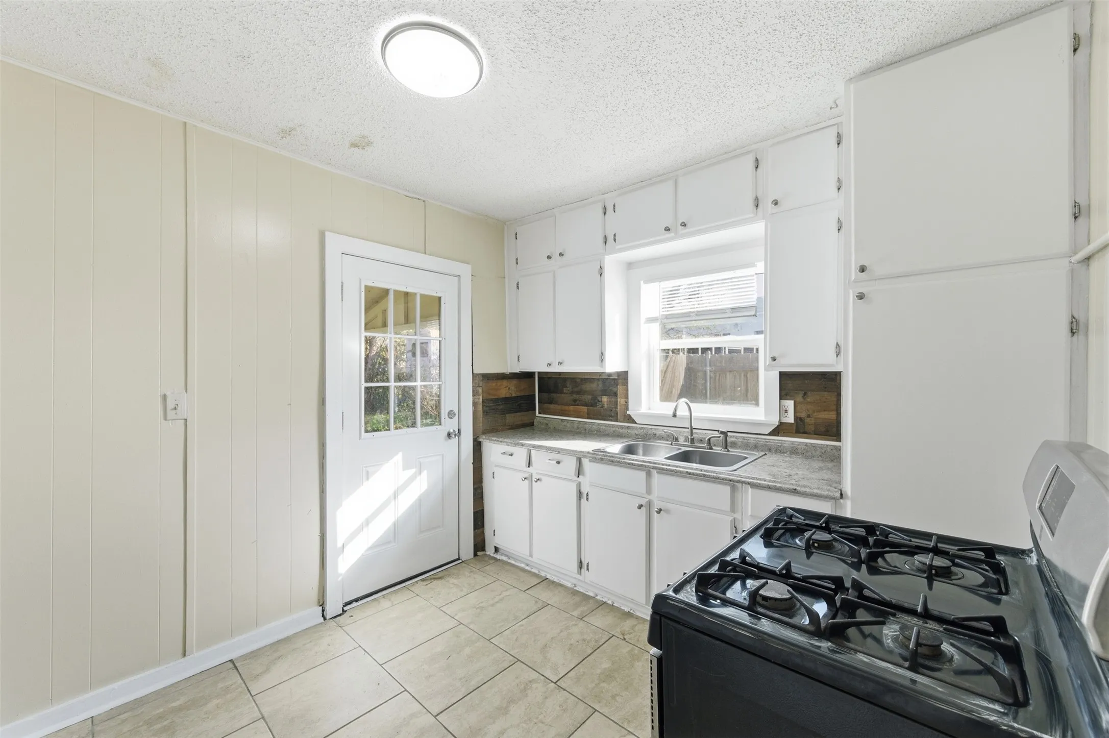 Kitchen featuring gas stove, white cabinets, light tile patterned flooring, a textured ceiling, and tasteful backsplash