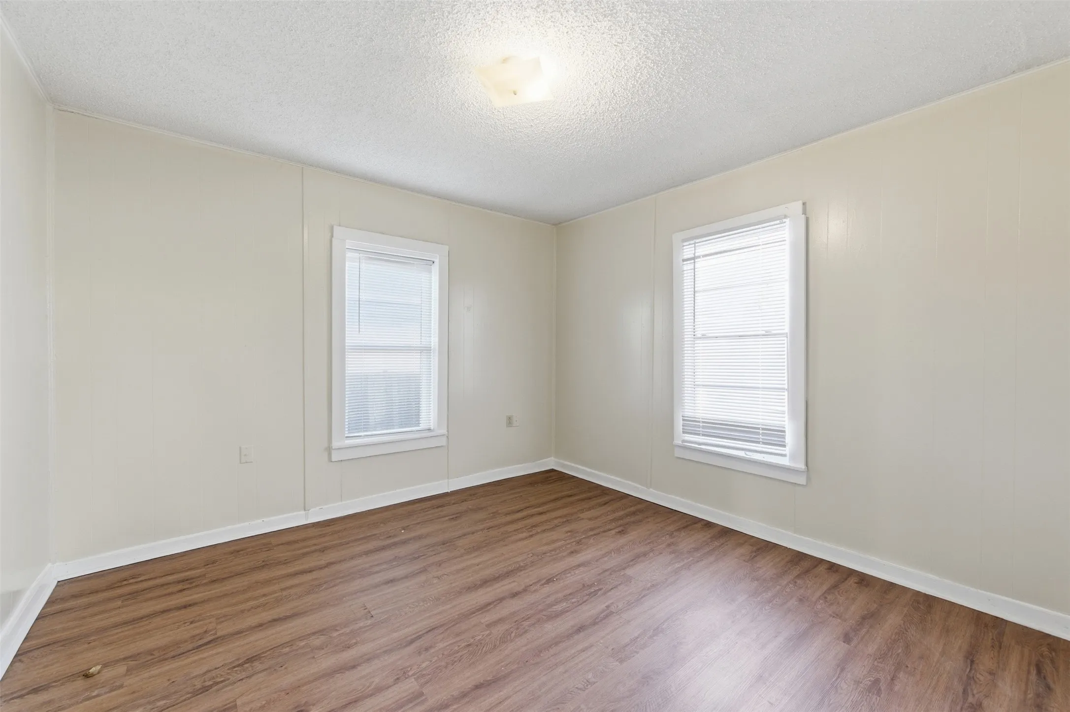 Unfurnished room with wood finished floors, healthy amount of natural light, and a textured ceiling