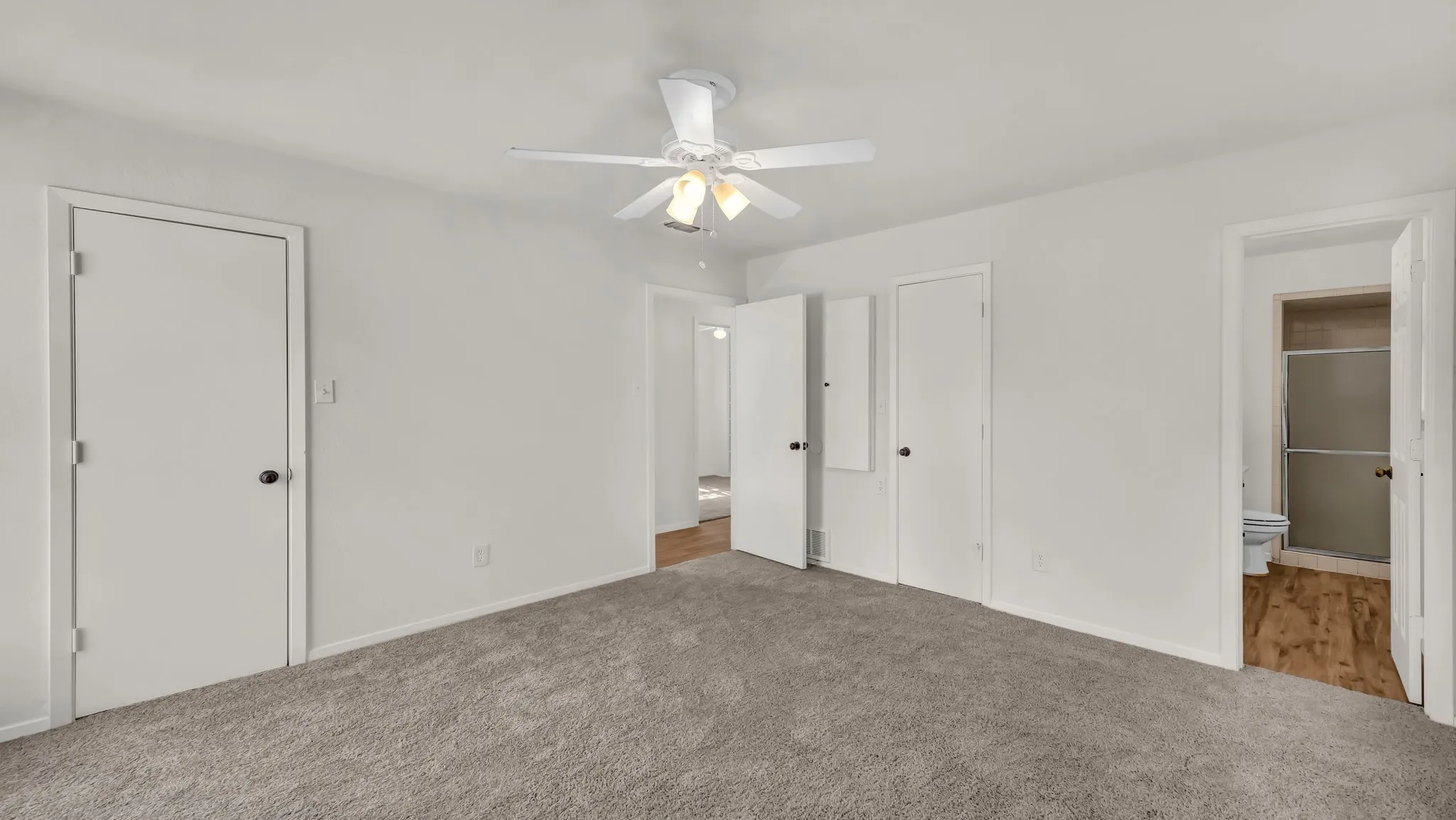 Unfurnished bedroom with connected bathroom, two closets, carpet, and ceiling fan