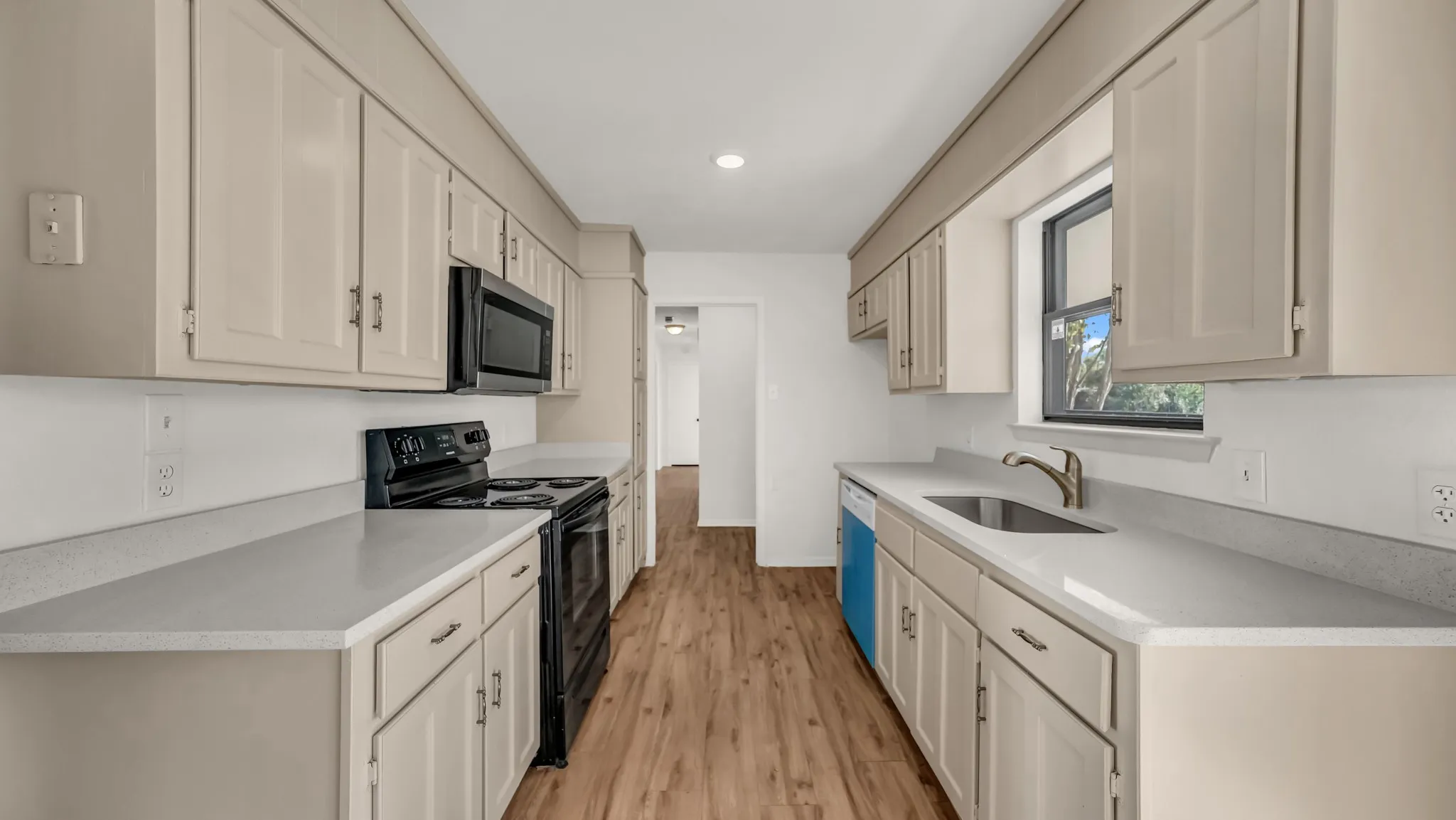 Kitchen with black electric range, light wood-style floors, stainless steel microwave, recessed lighting, and light stone countertops