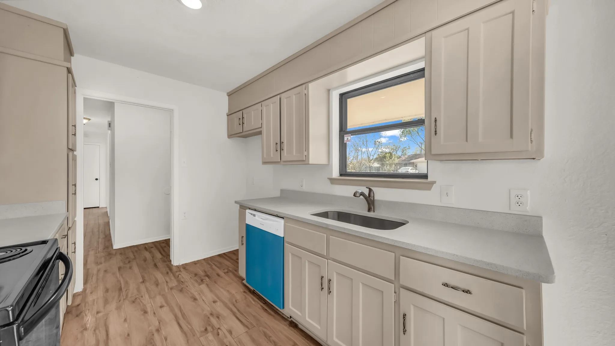 Kitchen with light wood finished floors, dishwasher, black range with electric cooktop, and light stone counters