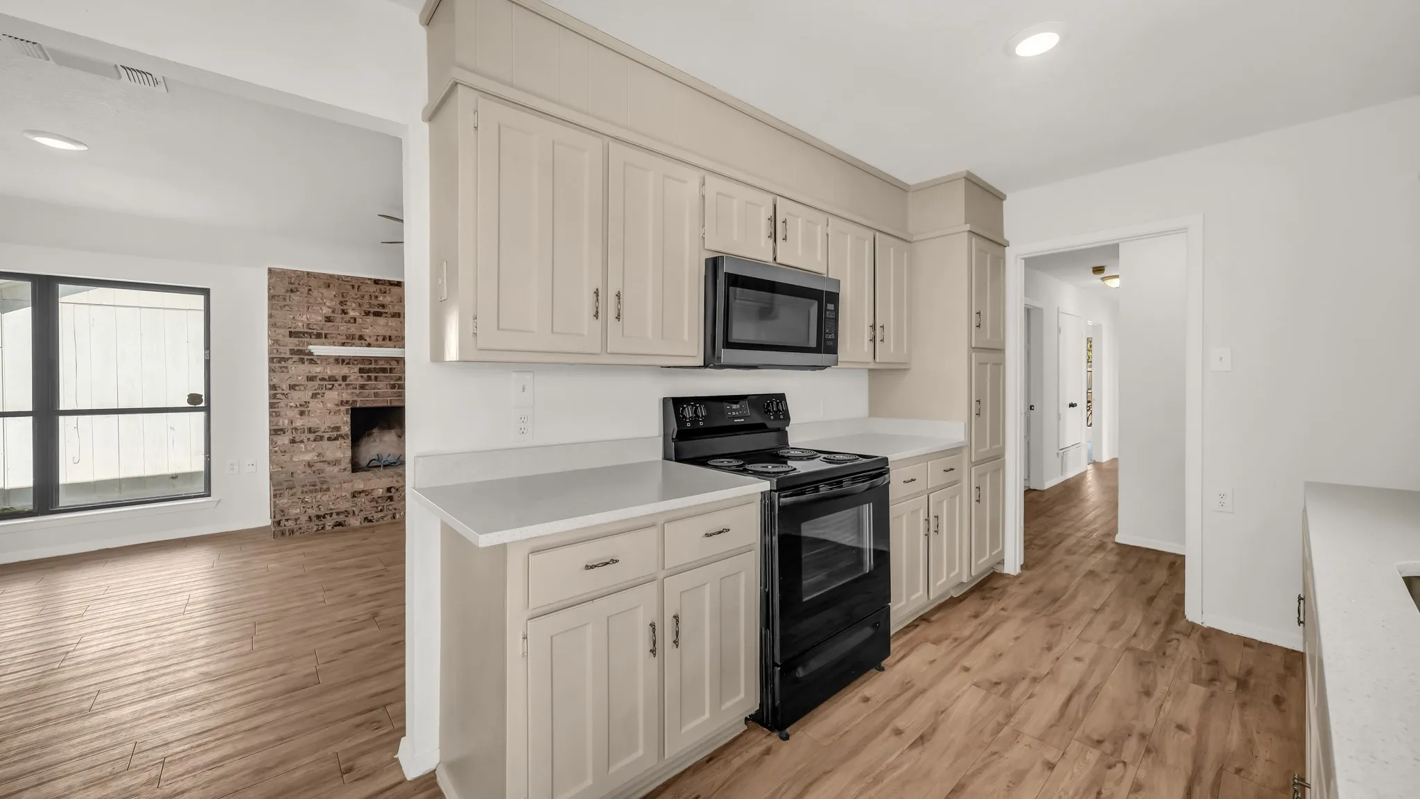 Kitchen with black electric range, recessed lighting, light countertops, stainless steel microwave, and light wood finished floors