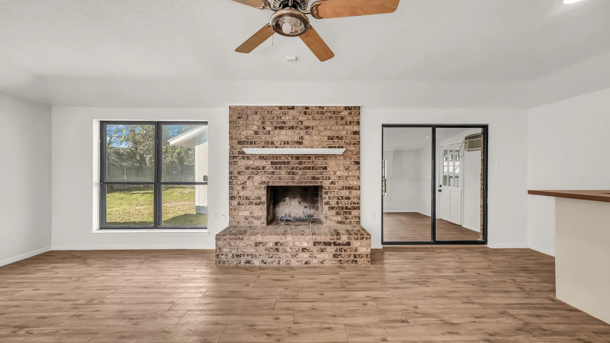 Unfurnished living room featuring wood finished floors, a brick fireplace, and ceiling fan