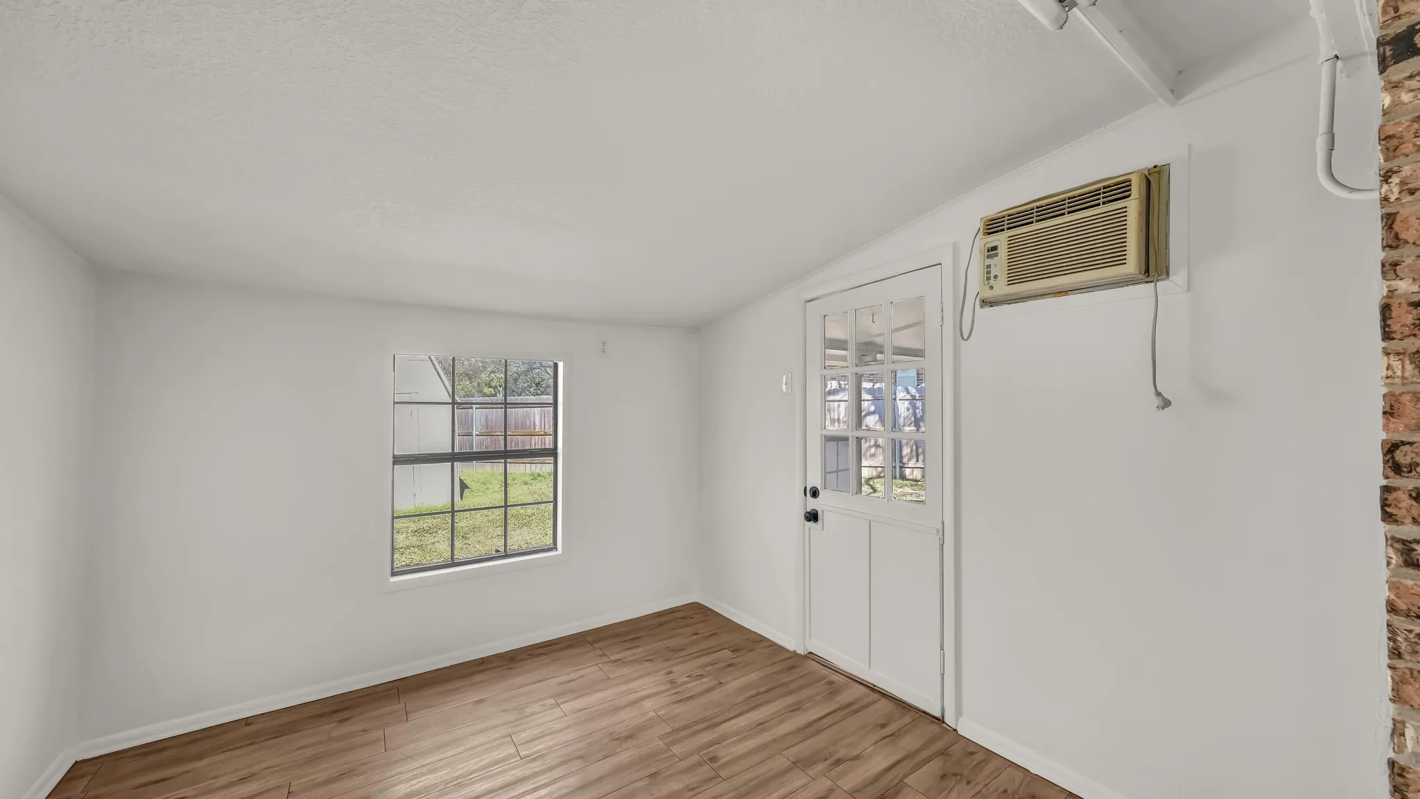 Entryway with light wood finished floors, a textured ceiling, vaulted ceiling, and an AC wall unit