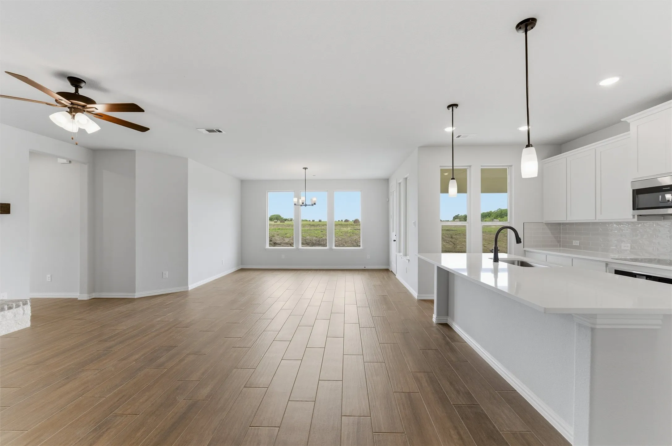 Kitchen featuring suspended lighting, wood tiled floors, a center island with sink, white cabinets, and light stone countertops