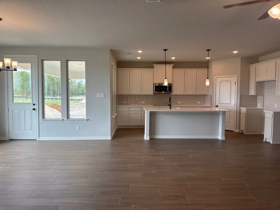 Kitchen featuring suspended lighting, wood tiled floors, a center island with sink, white cabinets, and light stone countertops