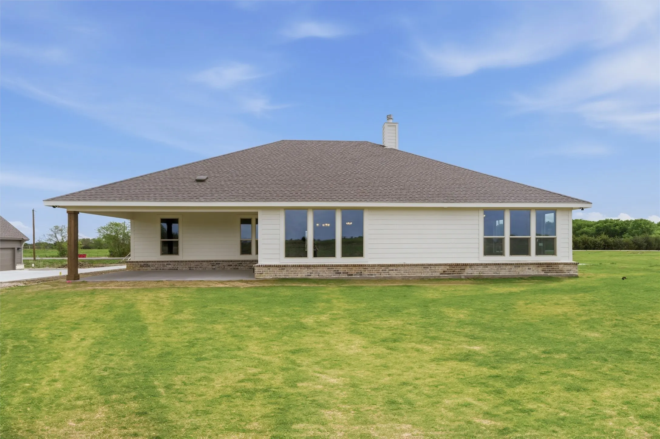 Back of house with brick siding, a yard, roof with shingles, a chimney, and a patio