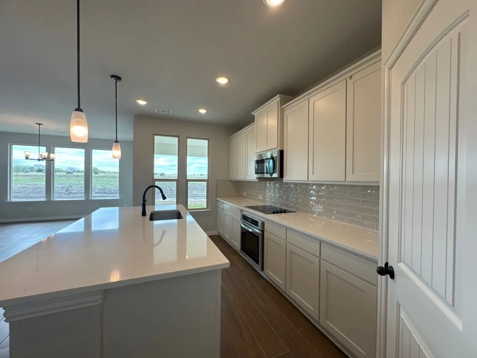 Kitchen featuring wood finish floors, an island with sink, stainless steel microwave, white cabinetry, and backsplash