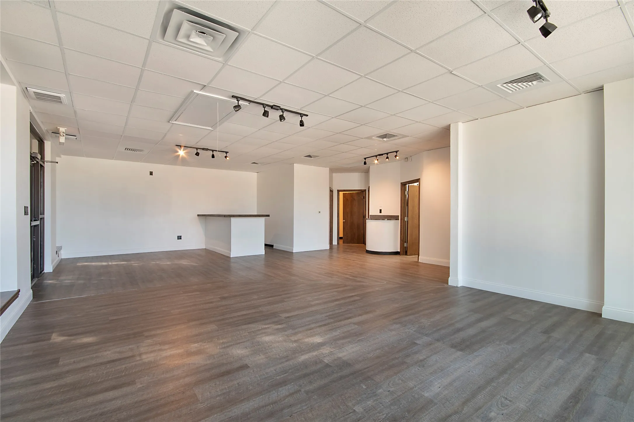 Empty room with track lighting, a drop ceiling, and dark wood-style flooring