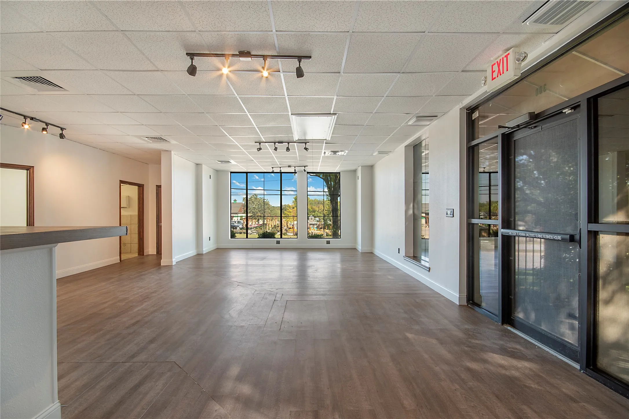 Empty room with track lighting, floor to ceiling windows, dark wood-type flooring, and a paneled ceiling