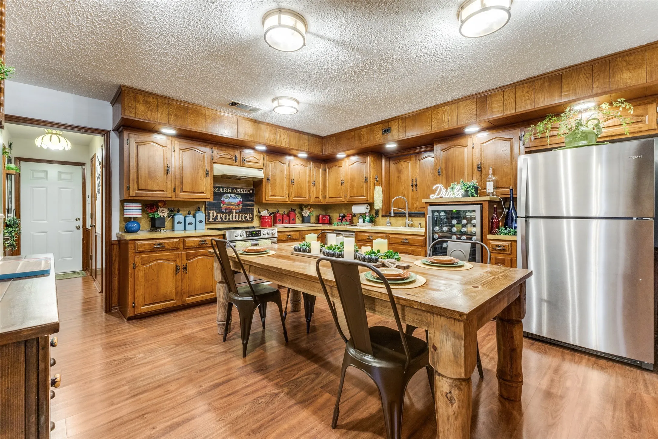 Kitchen with stained cabinets, freestanding refrigerator (which conveys with the home), light wood-style flooring and lots of light from fixtures and from under cabinet lights.