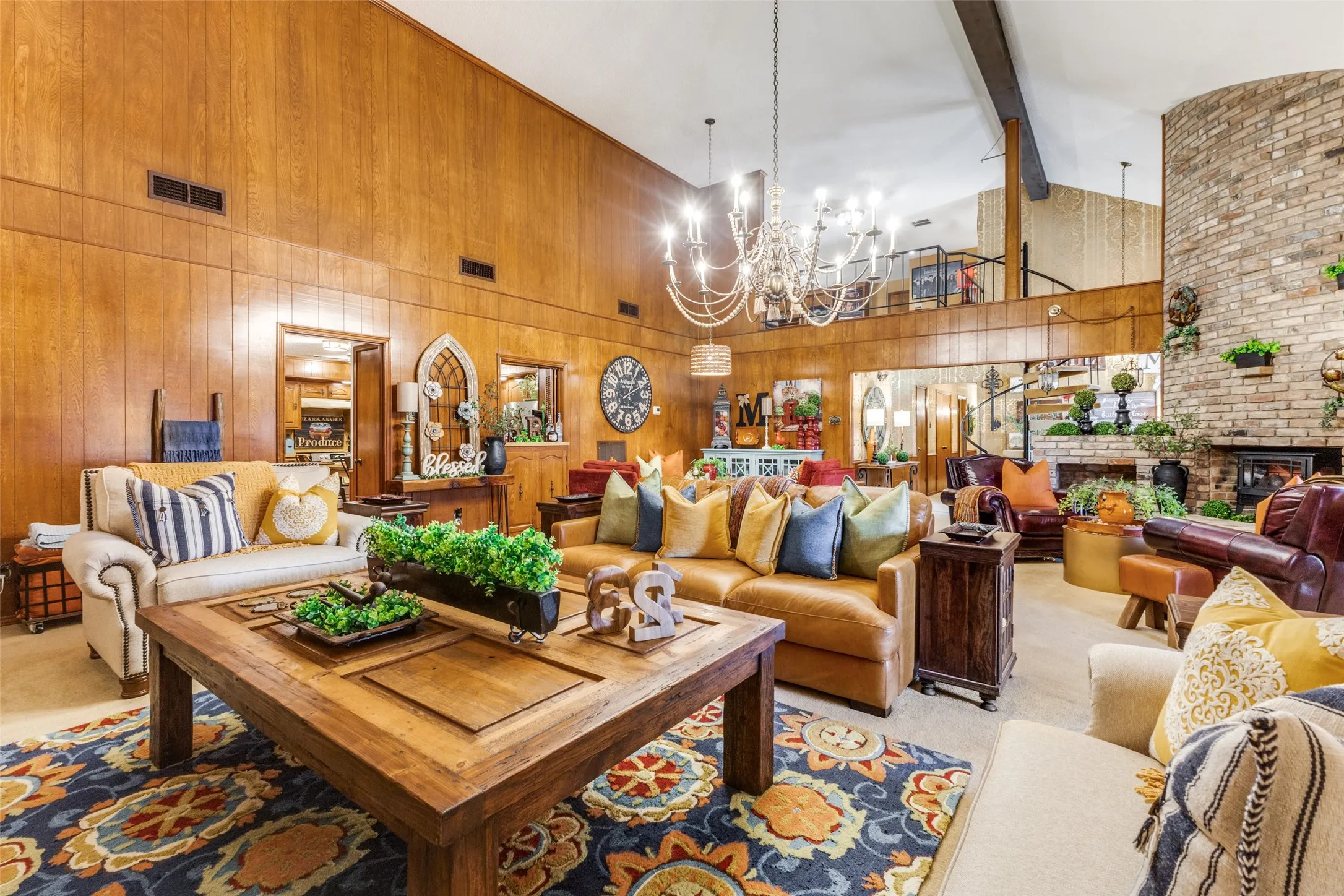 Living area featuring a high ceiling, carpet flooring, wooden walls, a chandelier, and a brick fireplace