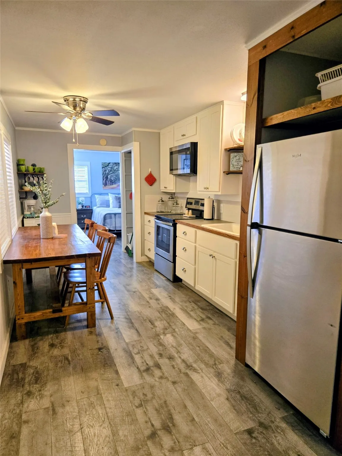 Kitchen with appliances with stainless steel finishes, open shelves, white cabinets, light countertops, and light wood-style flooring