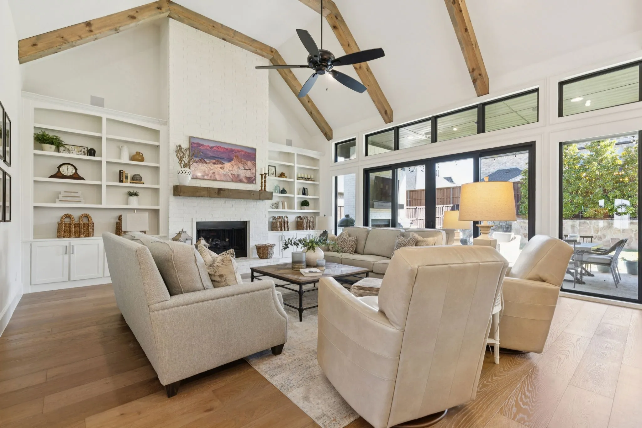 Living area with high vaulted ceiling, beam ceiling, a brick fireplace, wood finished floors, and a ceiling fan
