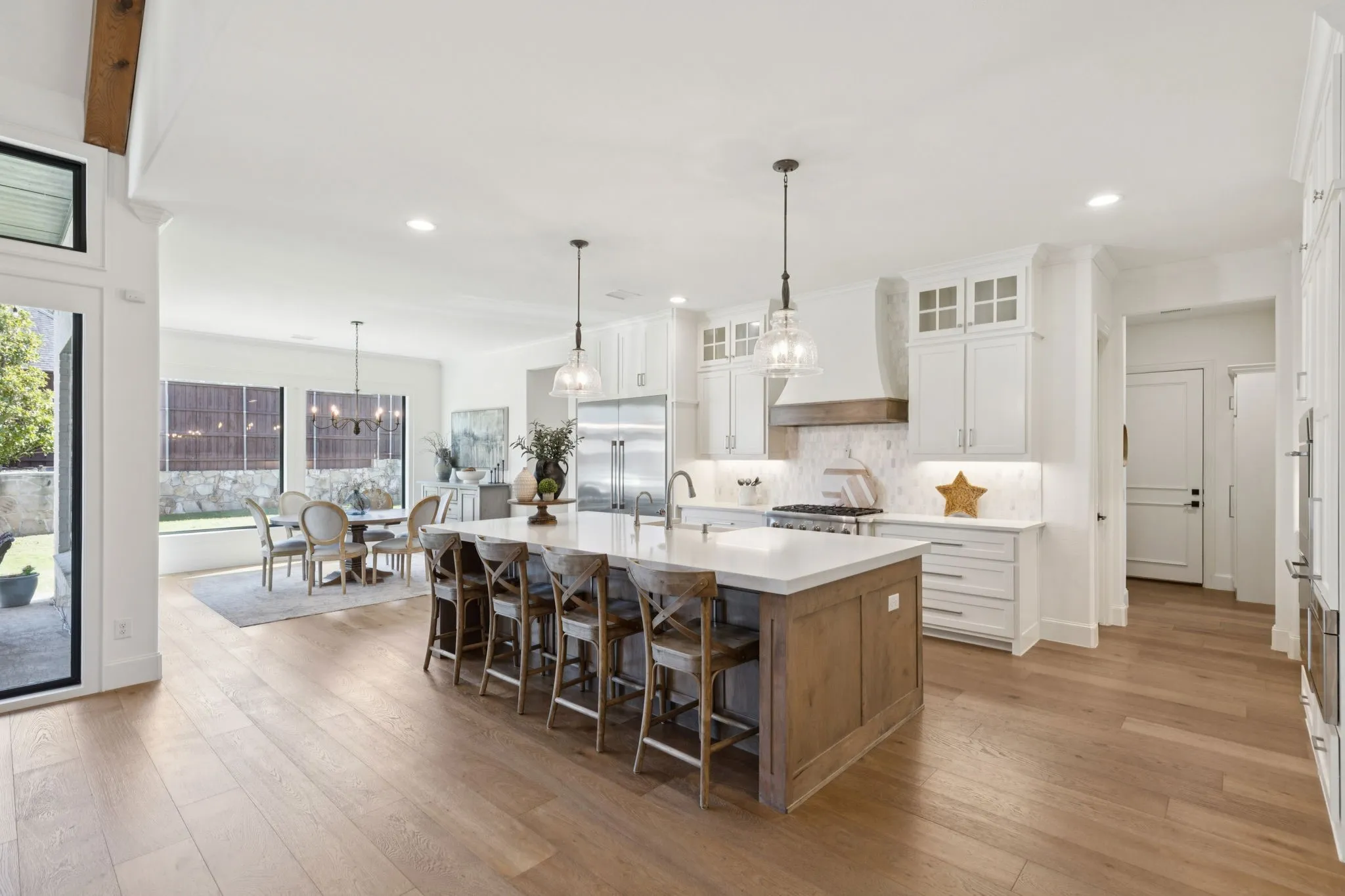 Kitchen with glass insert cabinets, backsplash, white cabinetry, a kitchen island with sink, and a kitchen bar