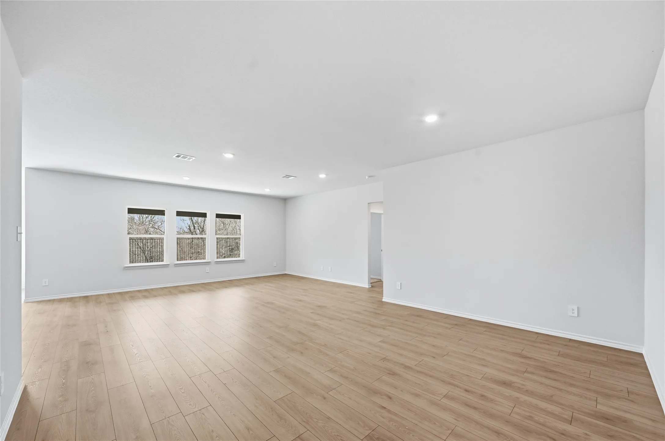 Expansive room featuring wood-finish flooring, recessed lighting, and a row of three windows