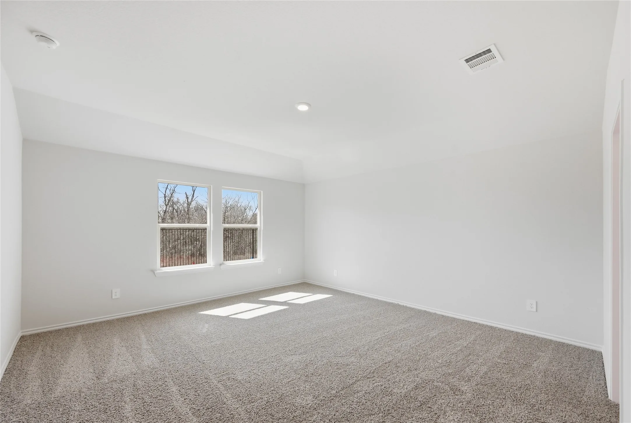 Spacious room featuring neutral carpeting, light-colored walls, and two large windows offering views of exterior trees