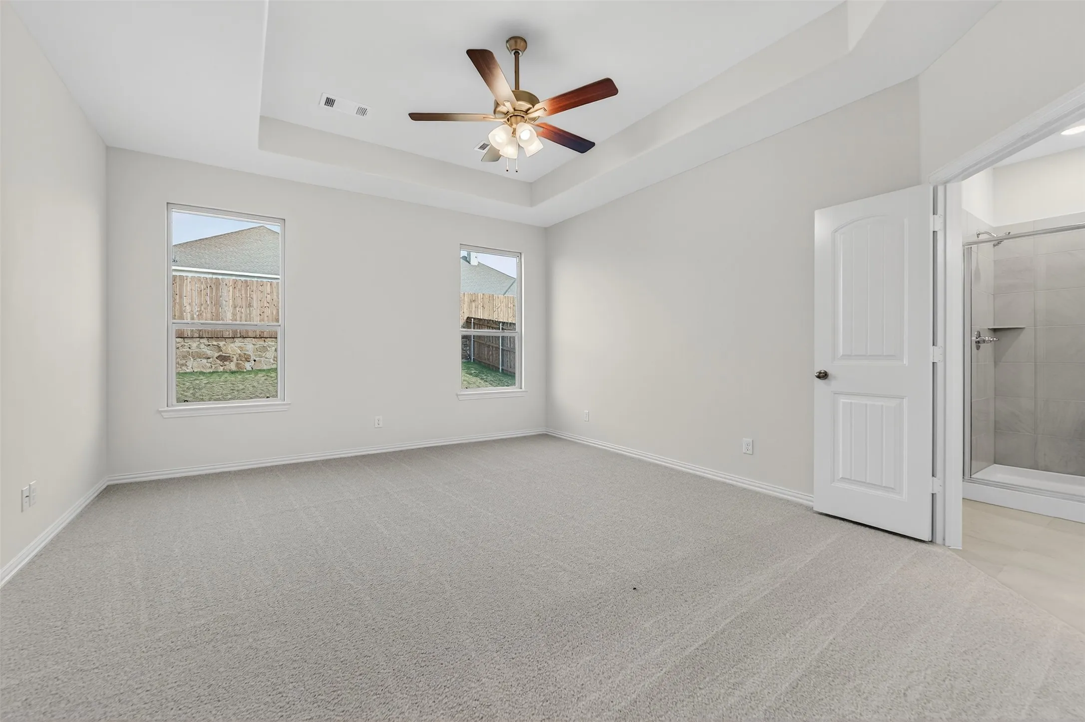 Spare room featuring a raised ceiling, light colored carpet, and ceiling fan