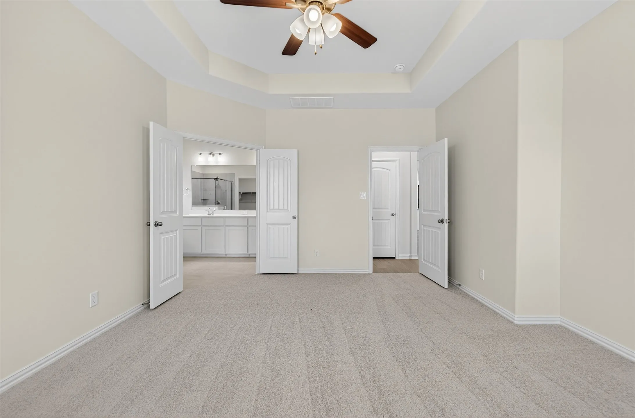 Unfurnished bedroom featuring light colored carpet, a raised ceiling, ceiling fan, ensuite bath, and a high ceiling